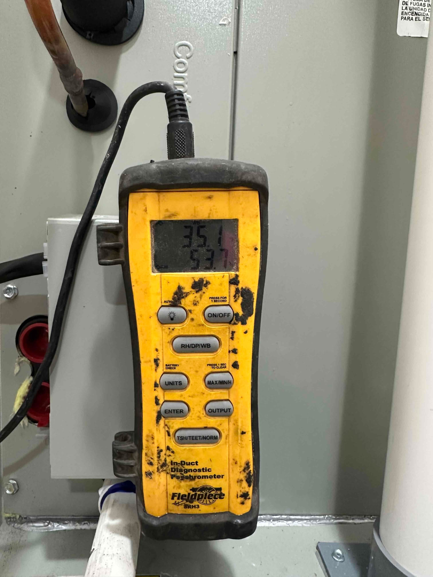 Digital in-duct thermometer displays 53.7°F, documenting cooled supply air temperature during system commissioning.