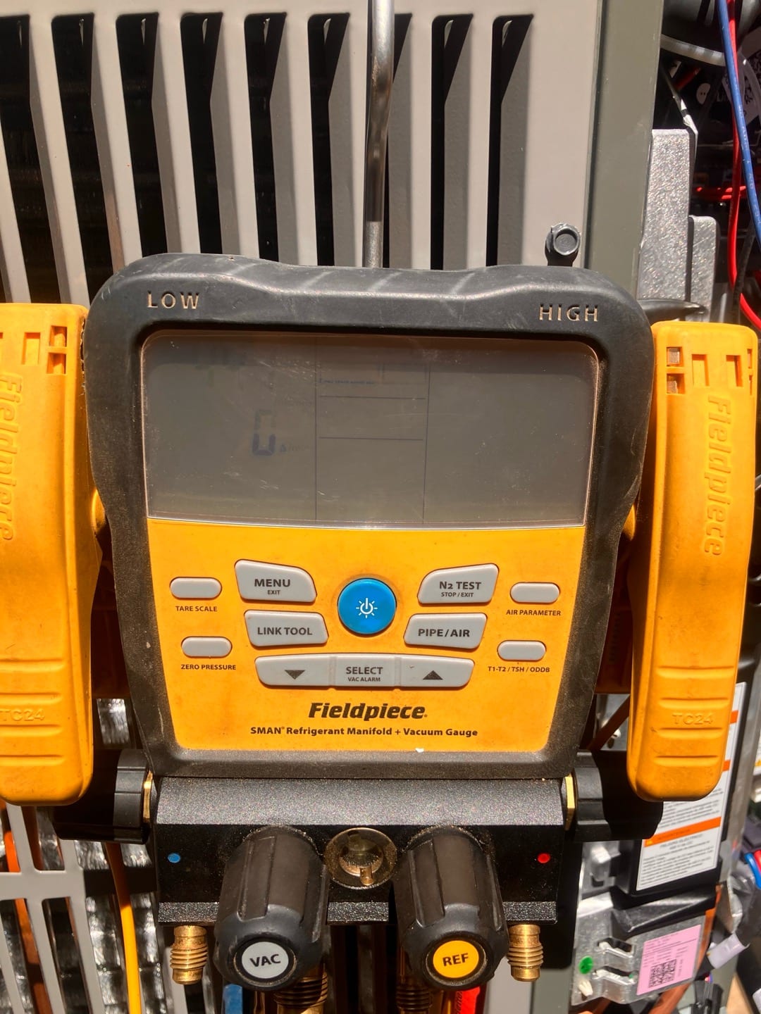 Digital refrigerant manifold with temperature clamp probes attached at an outdoor unit, screen not showing readable pressure or vacuum data.