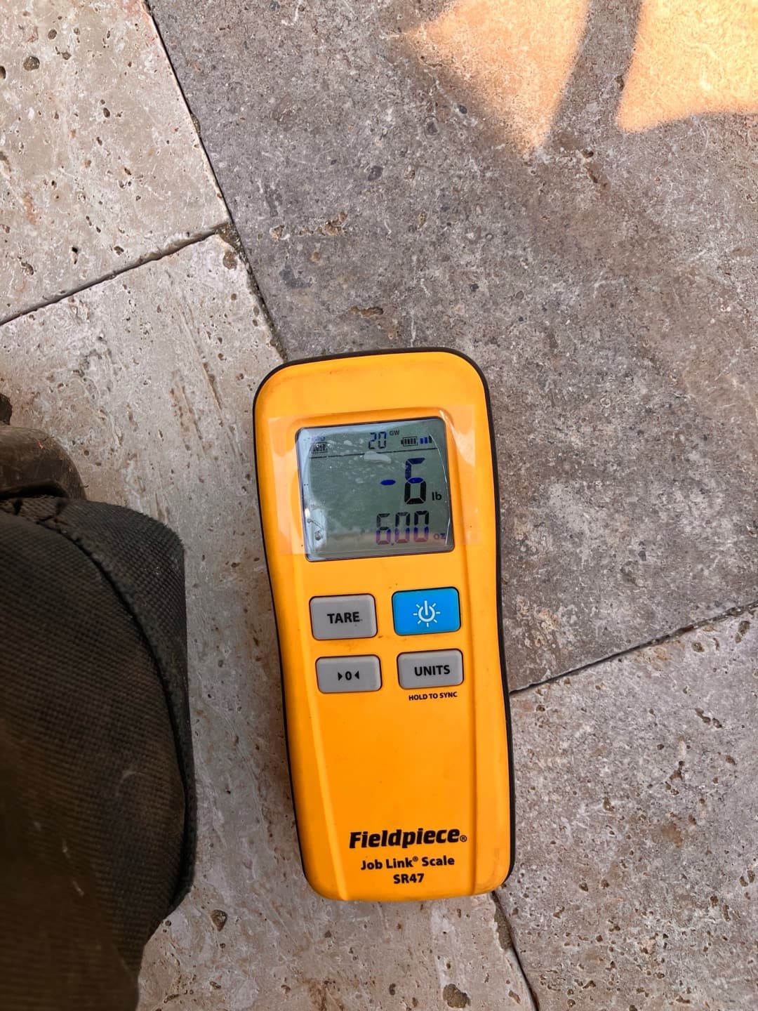 Digital refrigerant scale controller on the ground displays a negative weight reading and control buttons during system charging work.