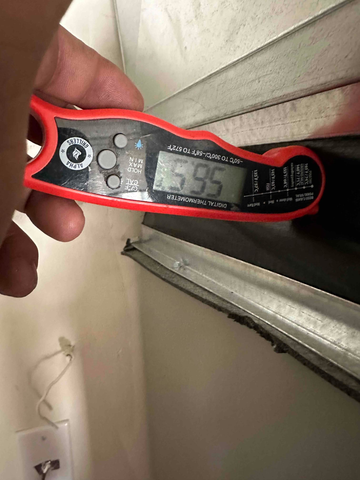 Digital thermometer at a duct opening reads 55°F, documenting supply air temperature during cooling performance check.