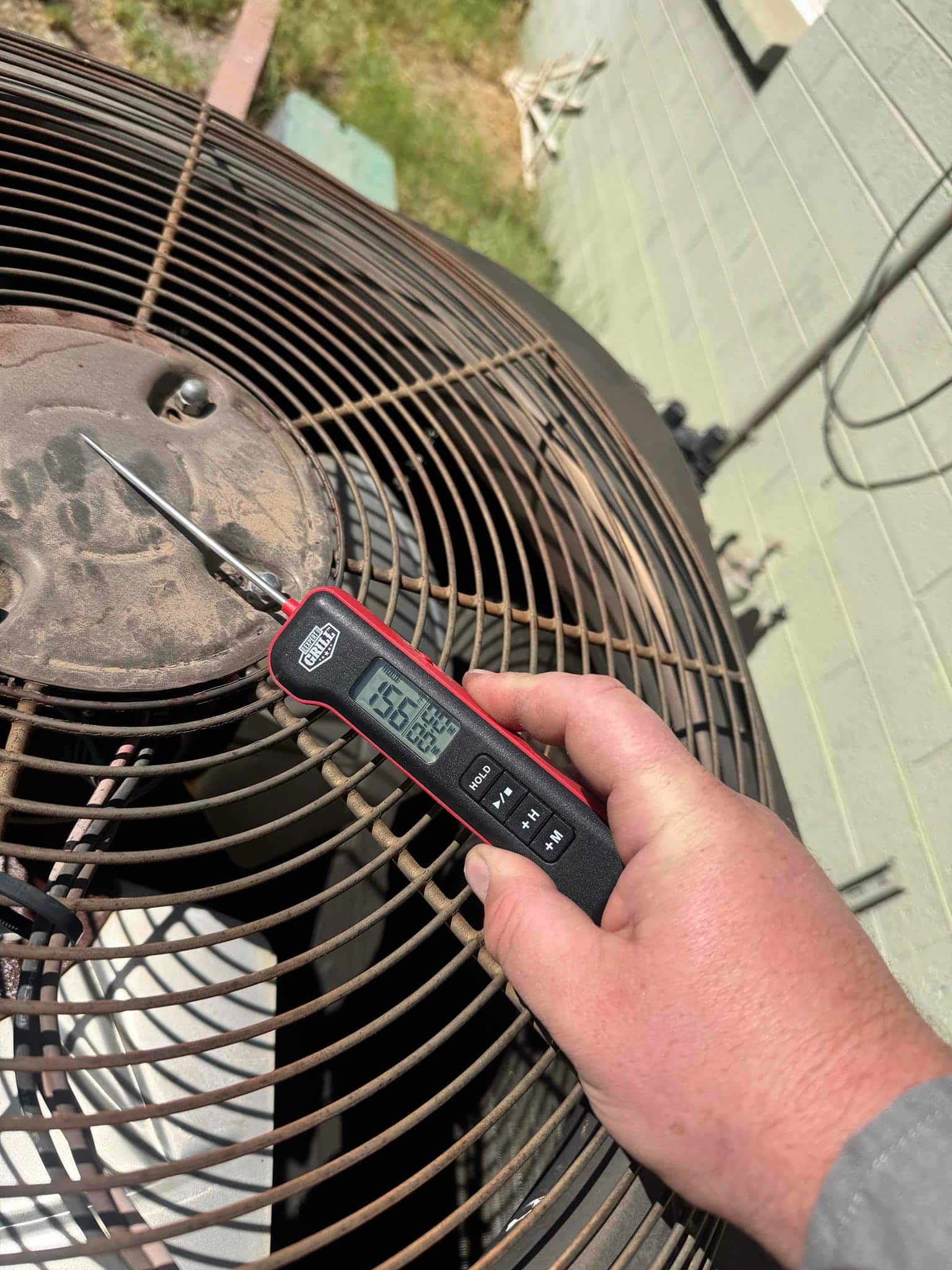 Digital thermometer measures 156.6°F on the condenser fan motor top plate while the outdoor unit operates.