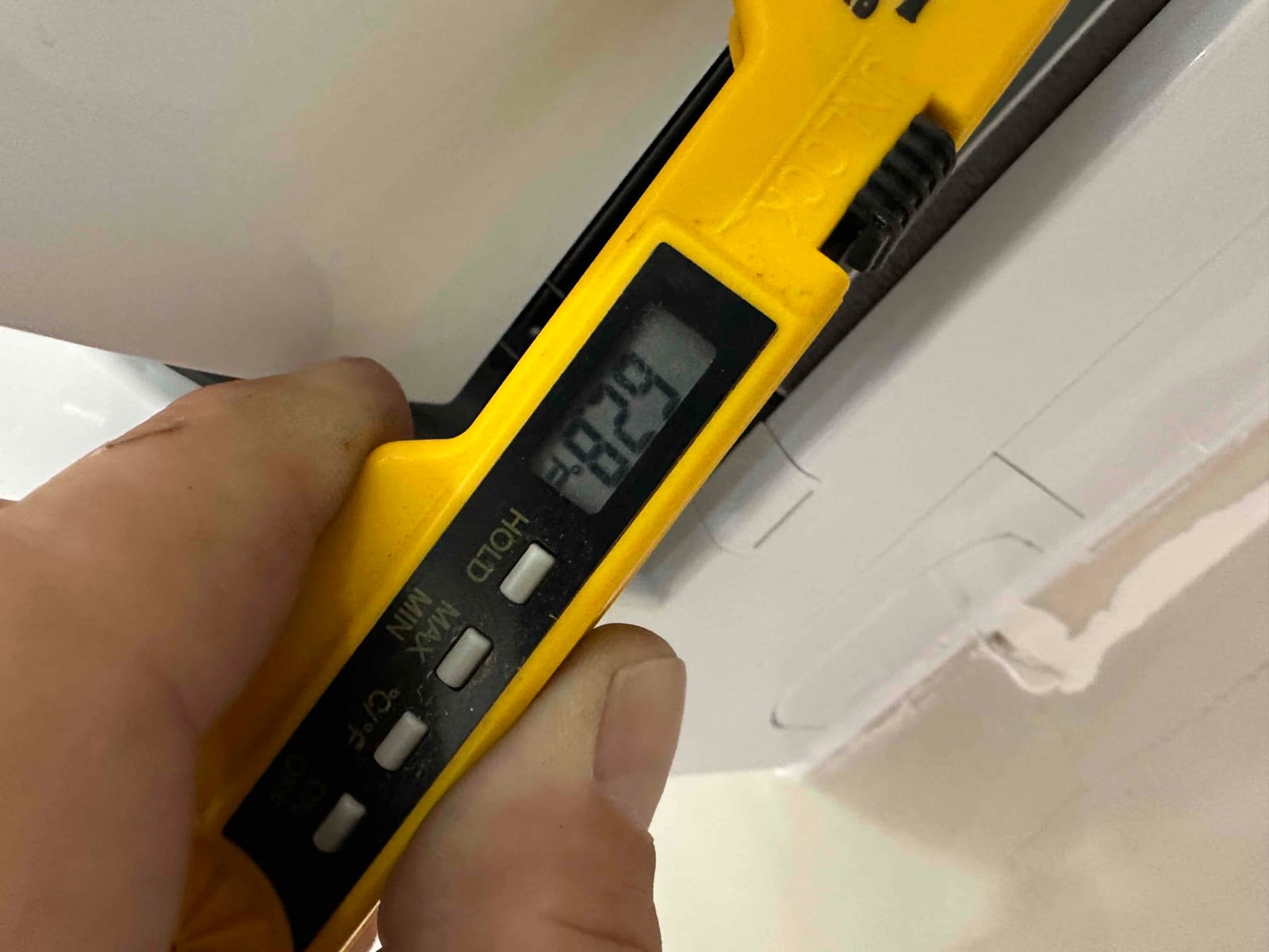 Digital thermometer probe measures air temperature at the indoor unit discharge during commissioning.