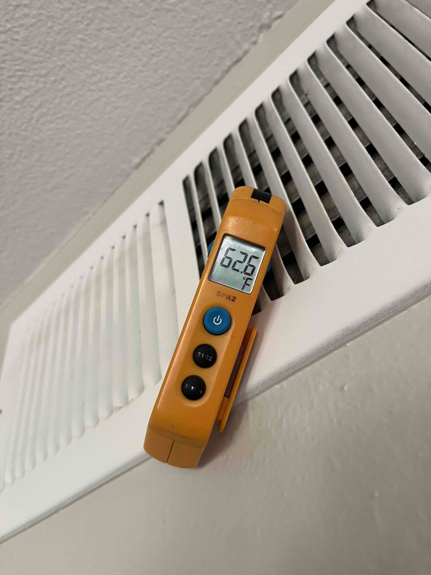 Digital thermometer shows 62.6 °F supply air temperature at a ceiling supply register during cooling operation.