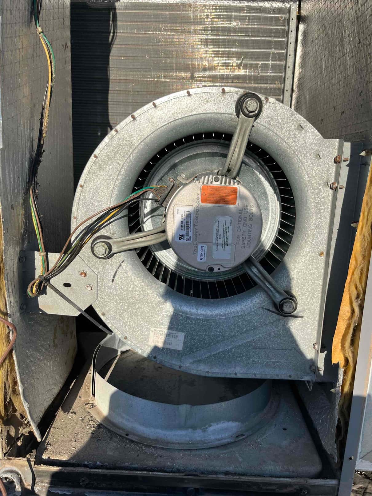 ECM blower motor and blower wheel assembly inside an air handler, showing metal housing, wiring harness, and surrounding insulation.