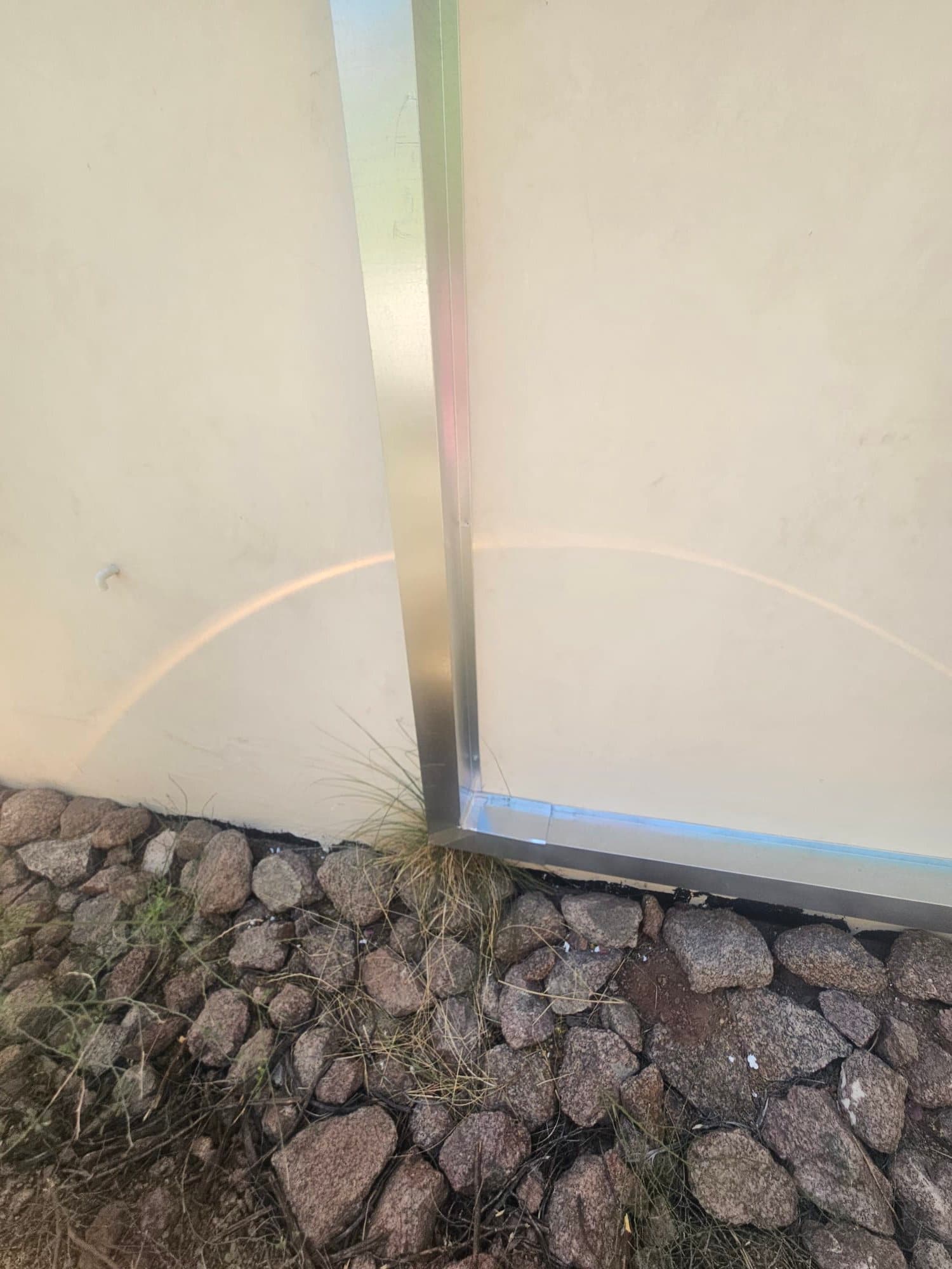 Exterior wall shows newly installed metal line set cover routed vertically and along the base, with sealed corner transition above landscaping rocks.