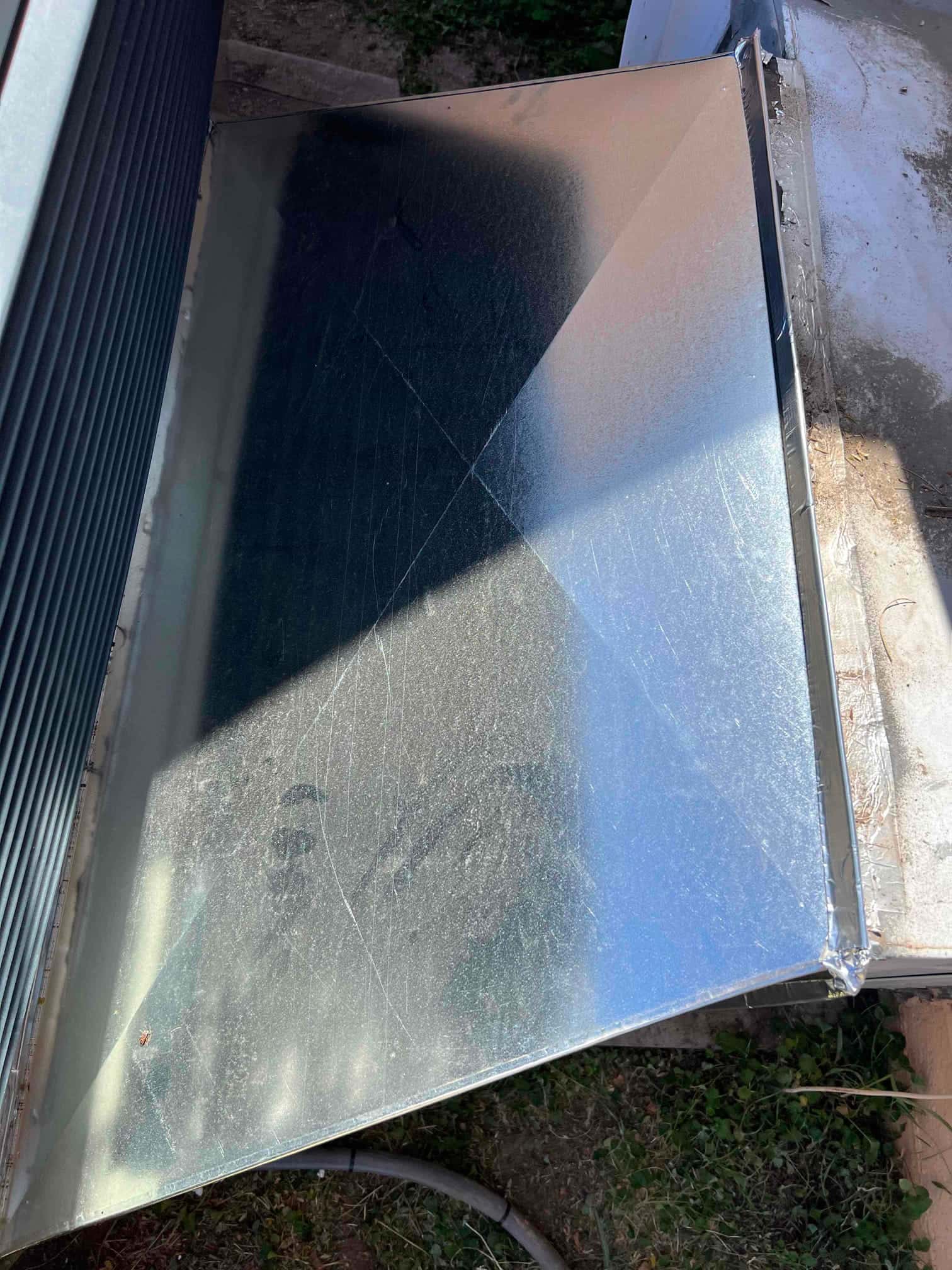 Freshly fabricated sheet metal transition connected at the outdoor unit, sealed at seams and set over the pad.
