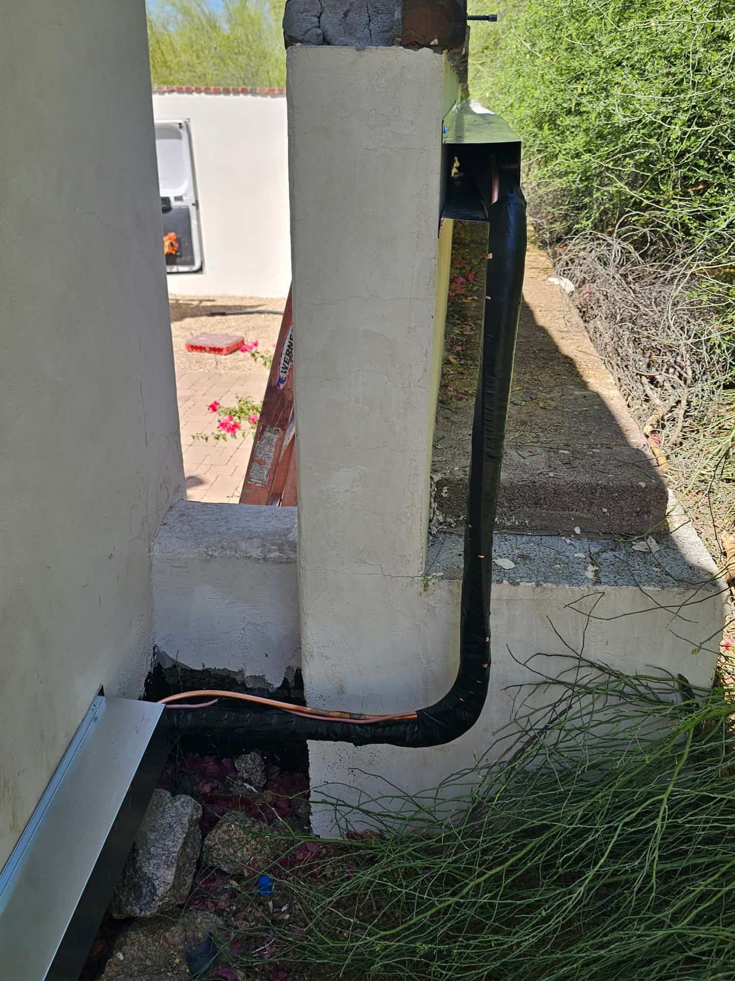 Insulated copper refrigerant line set routed along an exterior wall with protective cover and sealed wall penetration.