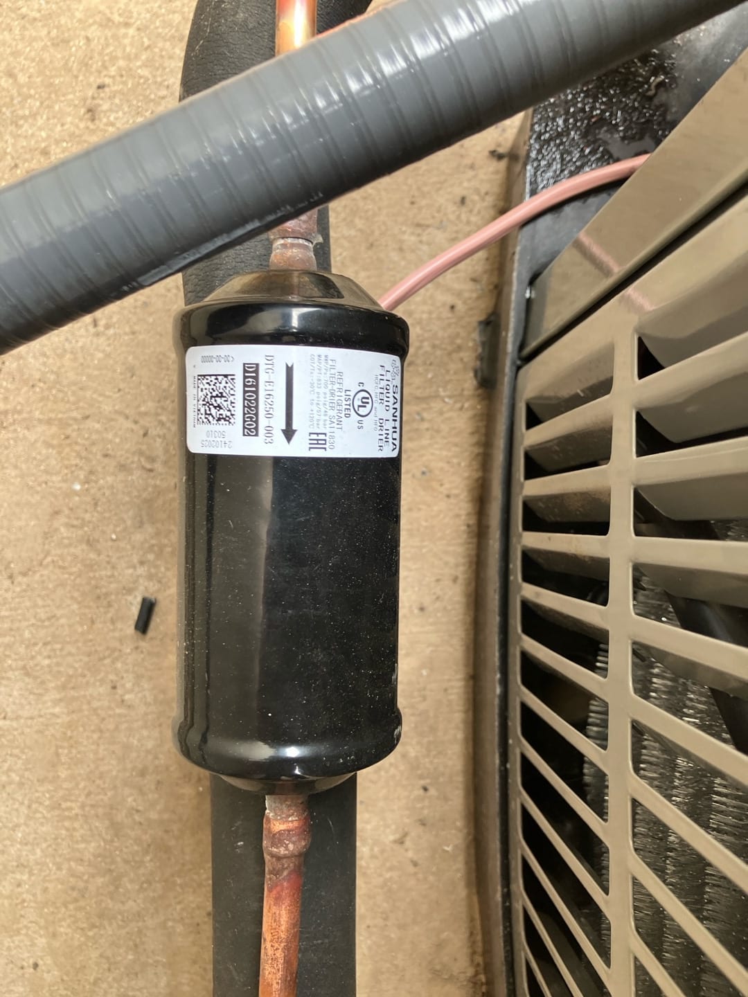 Liquid-line filter drier brazed into the copper tubing next to the outdoor condenser unit, with insulation and control wire visible.