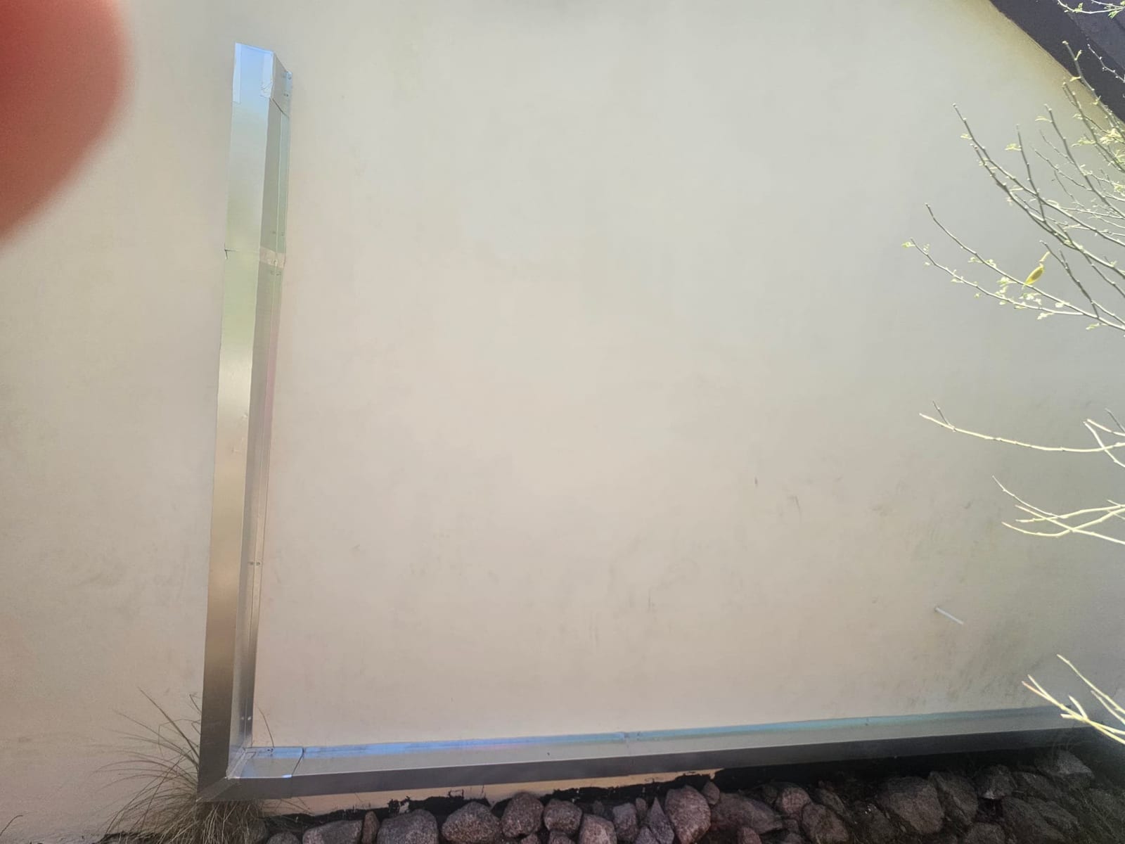 Metal line set cover installed along exterior wall with clean vertical and horizontal runs above landscape rocks.