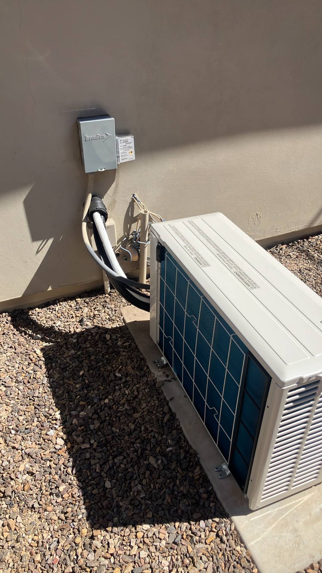 Mini-split outdoor unit set on a pad with insulated line set, electrical disconnect, and condensate drain routed along the wall.