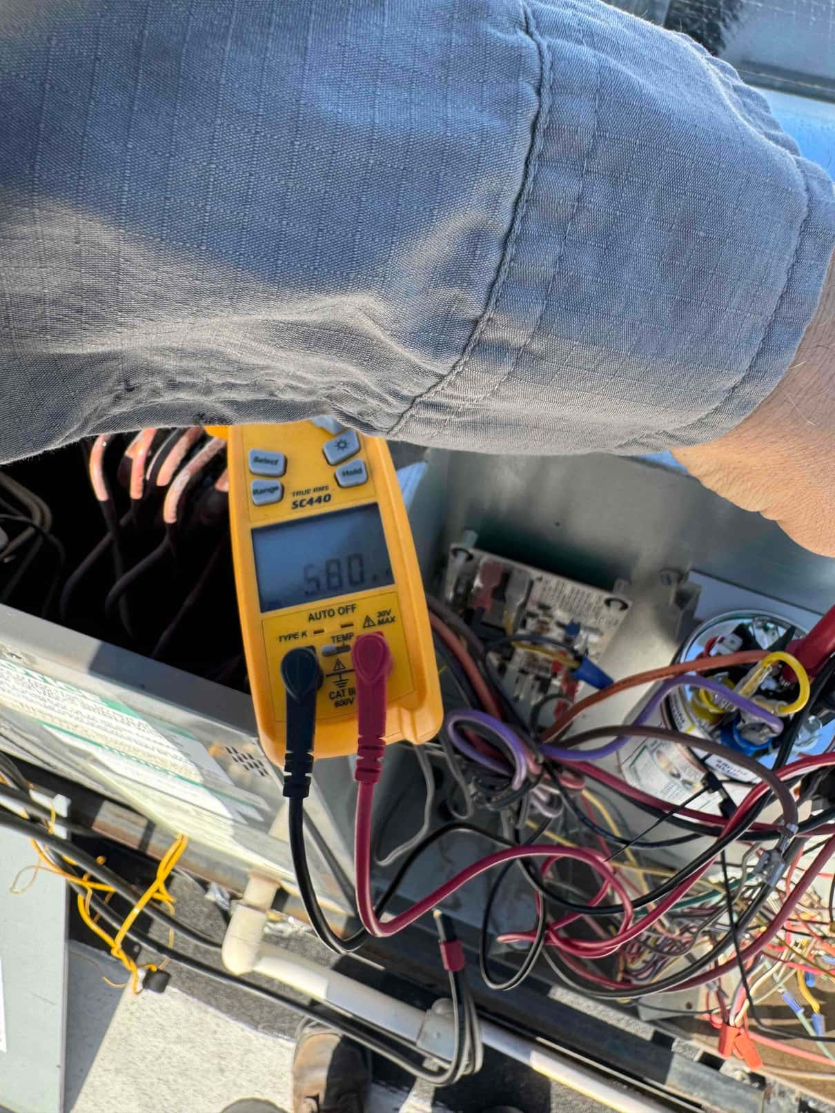 Multimeter measures capacitor at 5.80 µF with test leads connected inside the outdoor condenser control compartment.