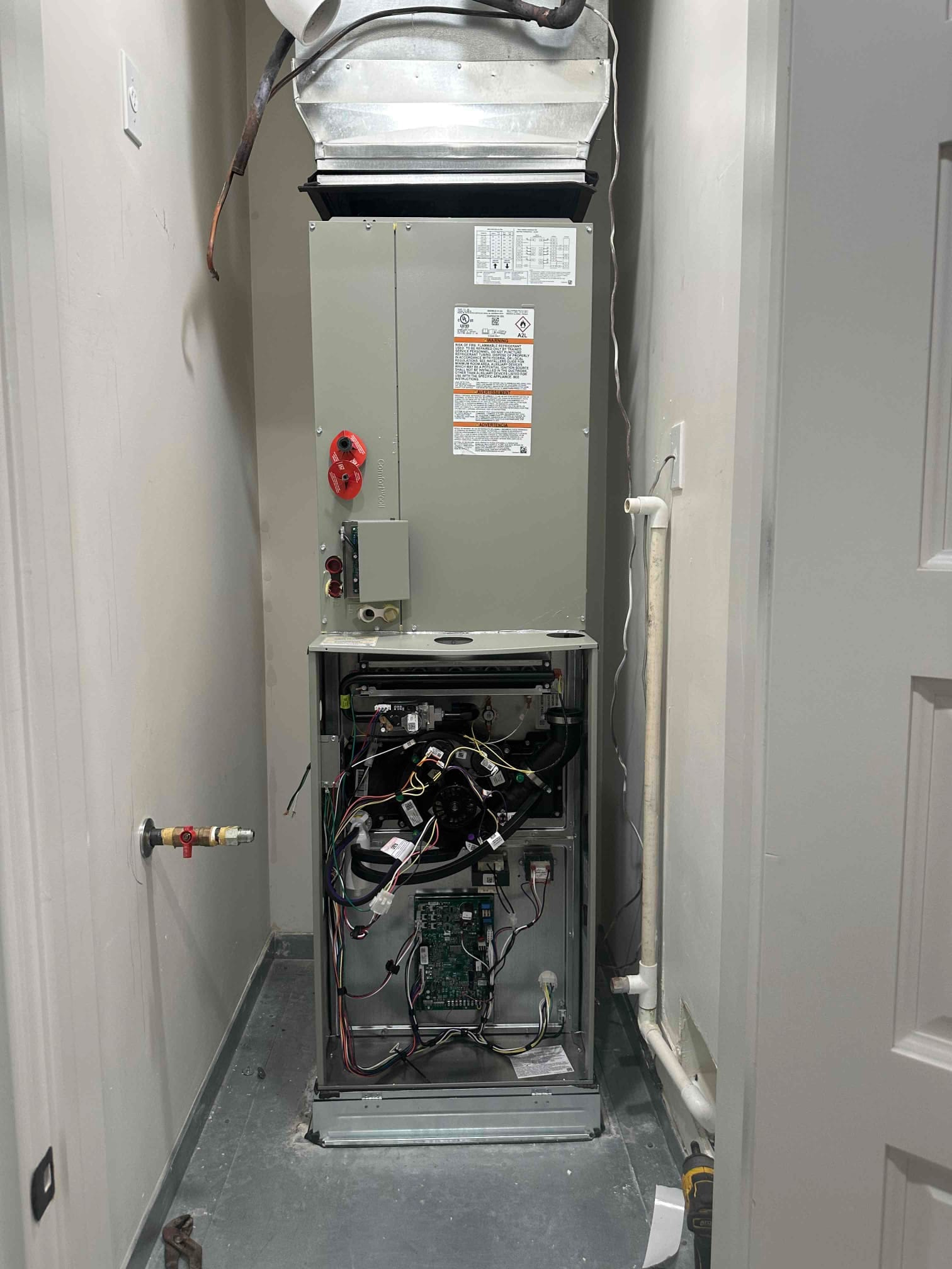 New air handler installed in closet with duct transition, condensate drain, gas line stub, and blower compartment open for wiring.