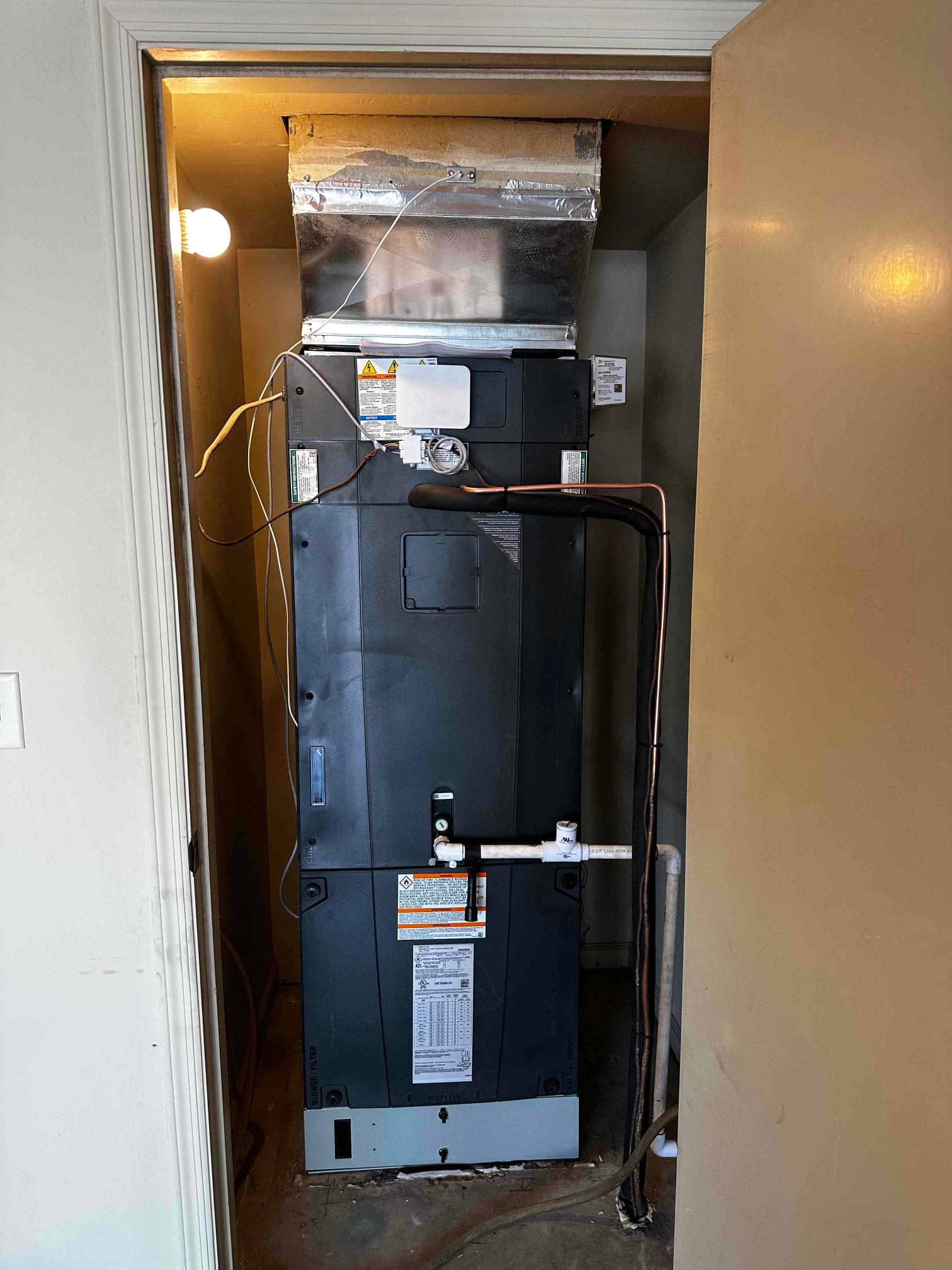 New air handler installed in a closet with insulated supply plenum, condensate drain piping, and refrigerant line connections.
