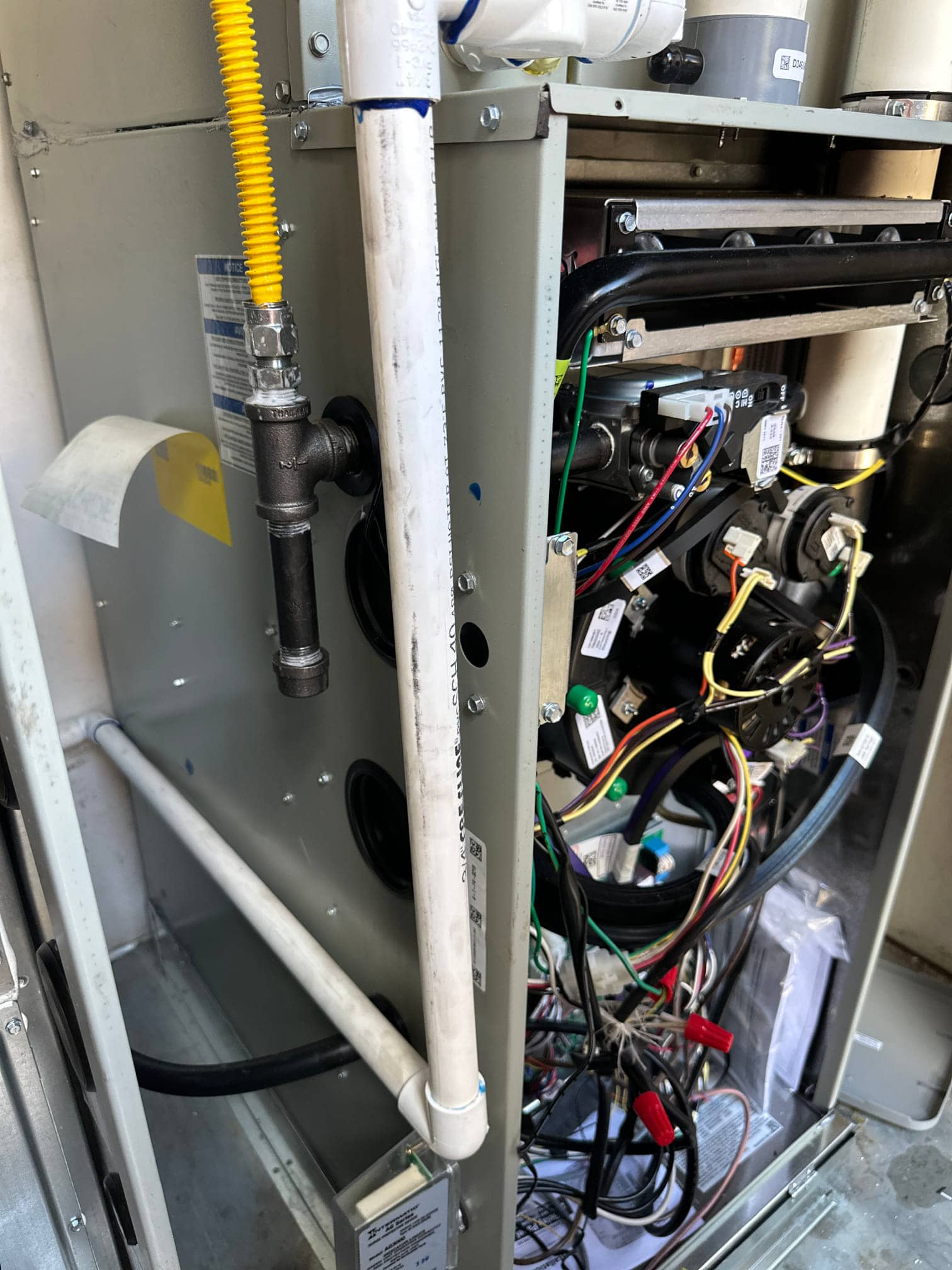 New furnace and coil cabinet with gas flex connector, condensate drain piping, and wiring routed inside the open service panel.