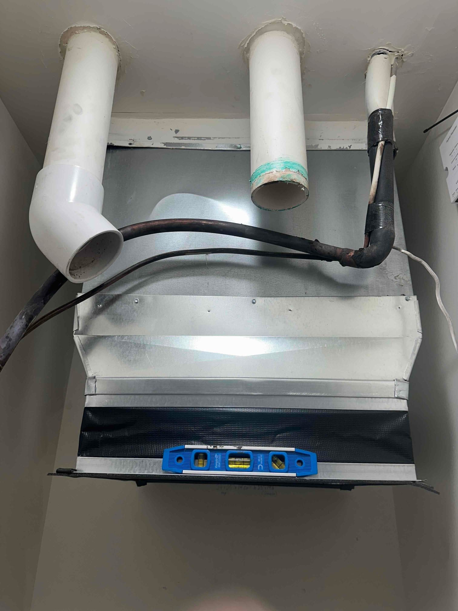 New furnace venting and refrigerant lines set above the air handler with sealed penetrations and a level used to check alignment.