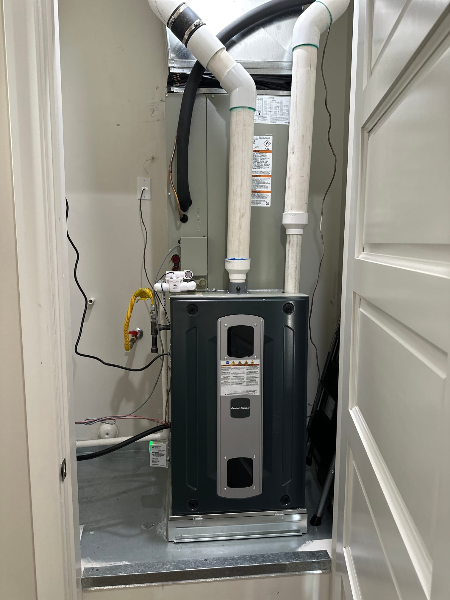 New gas furnace and coil set on a metal platform with PVC venting, condensate drain, gas flex, and electrical connections routed.