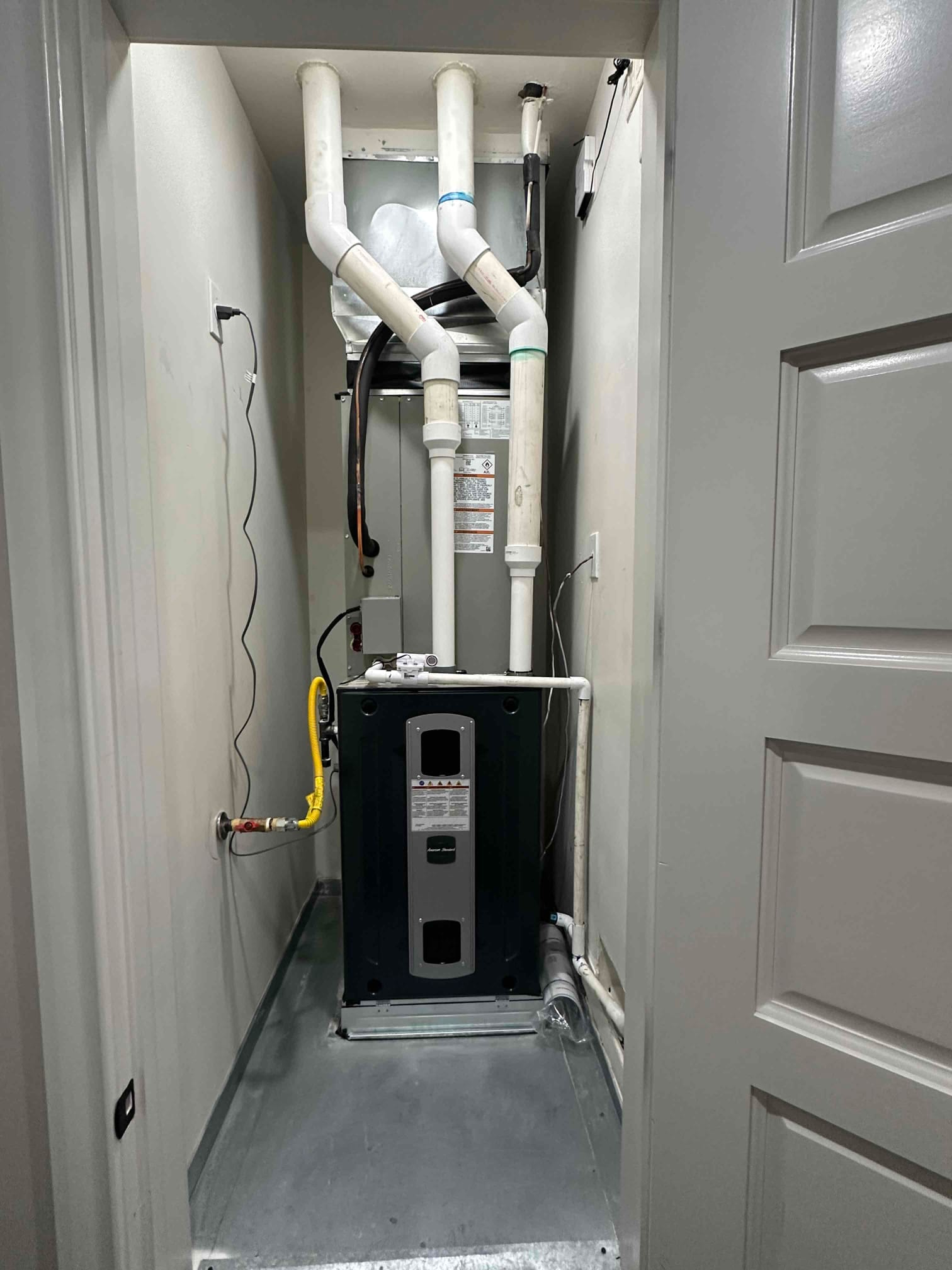 New gas furnace and evaporator coil installed in a closet with PVC venting, insulated refrigerant lines, condensate drain, and drip pan.