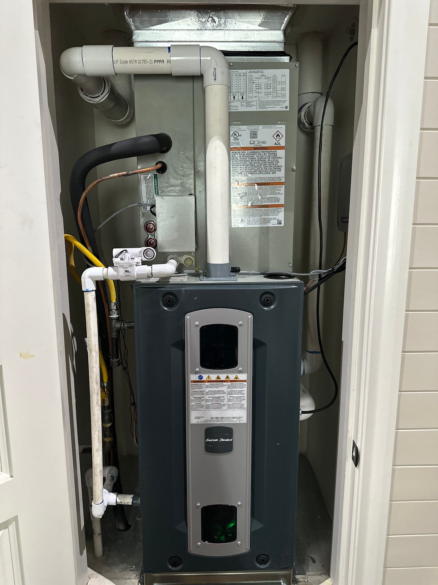 New indoor furnace and coil installed in a closet, with PVC condensate and vent piping, insulated refrigerant lines, and gas connection routed cleanly.