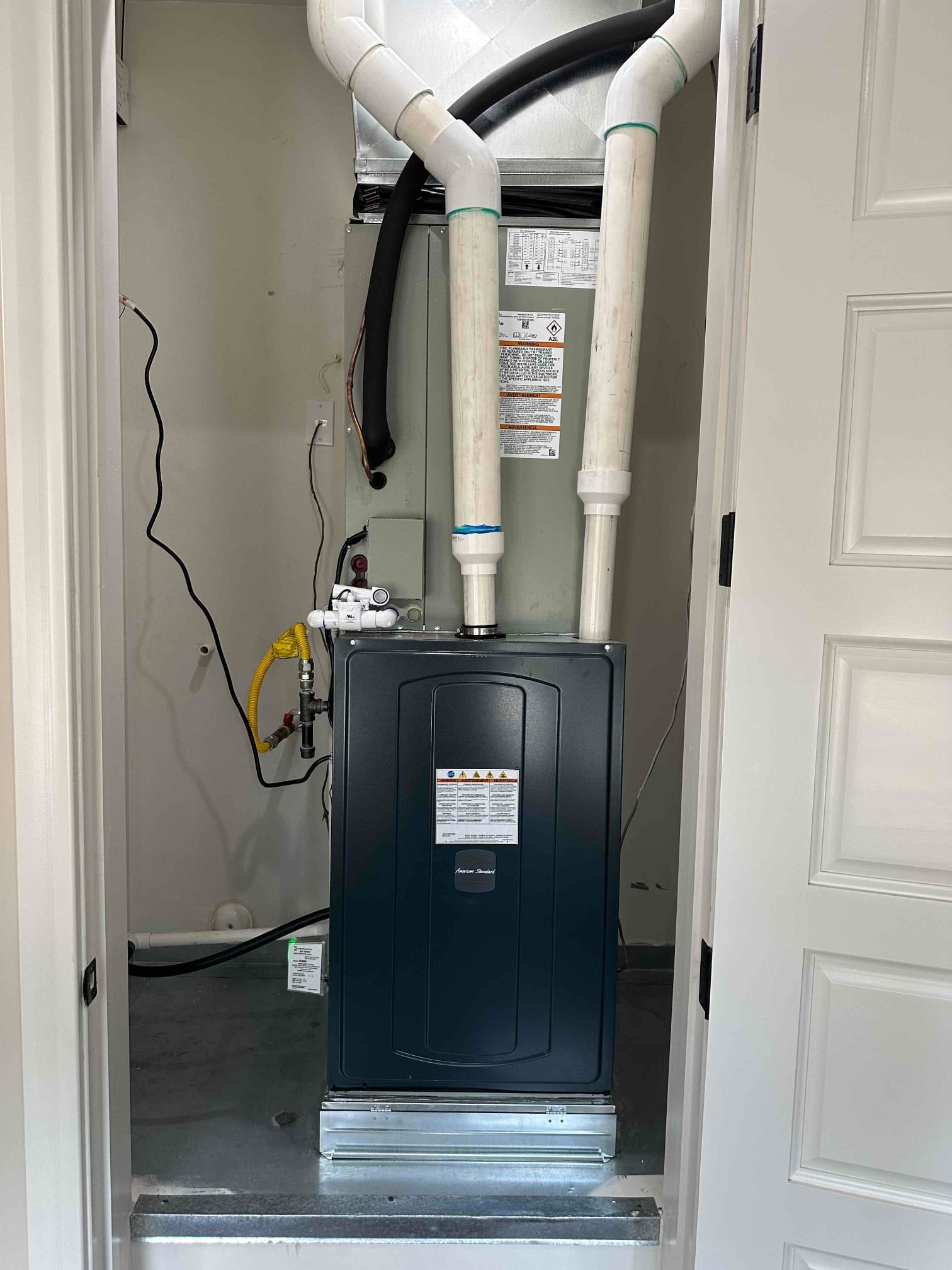 New indoor furnace and coil installed on a metal platform with PVC venting, condensate piping, gas line, and insulated refrigerant line.