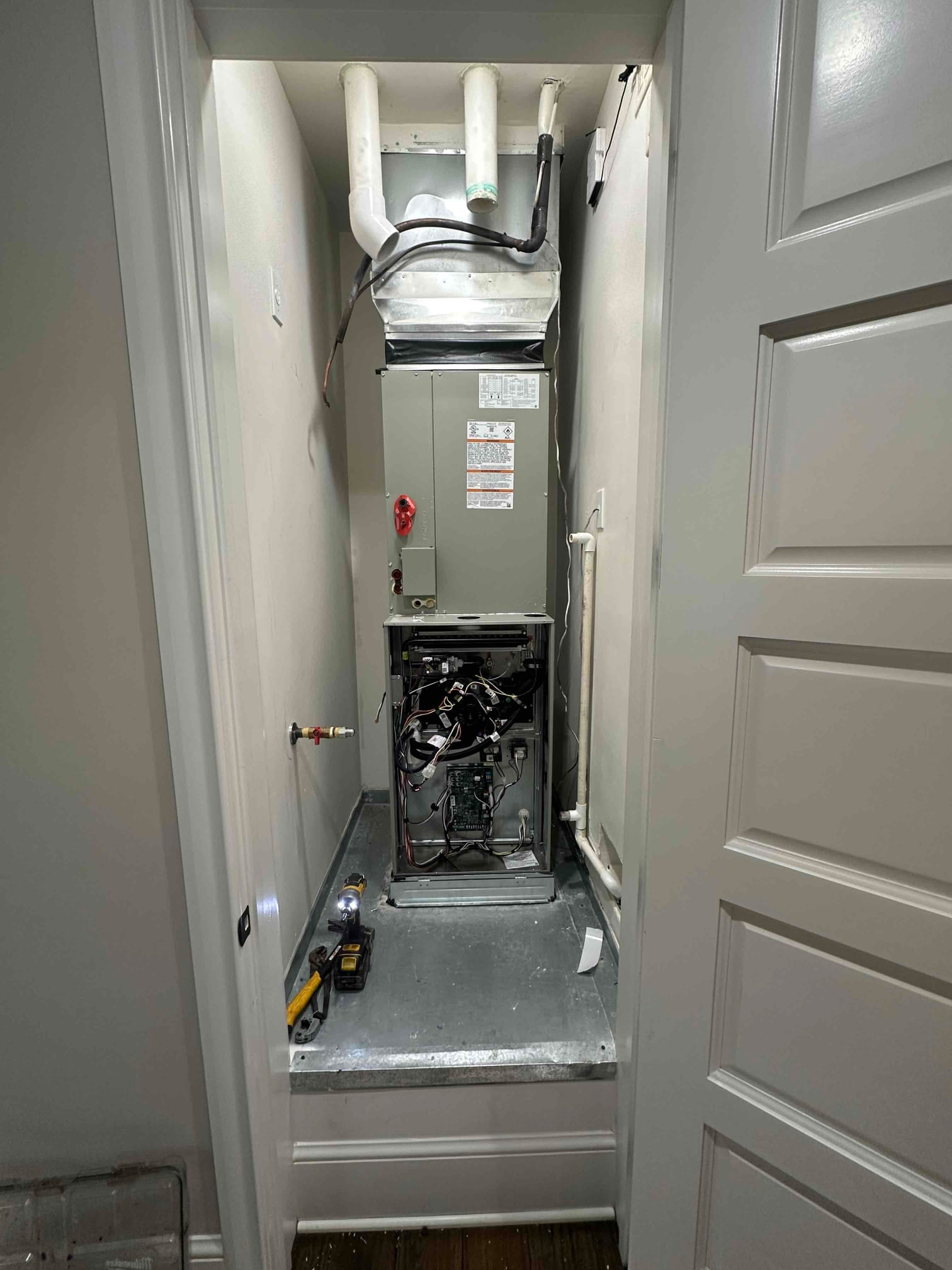 New indoor furnace and evaporator installed in a closet, with condensate piping, venting, and electrical compartment open during setup.