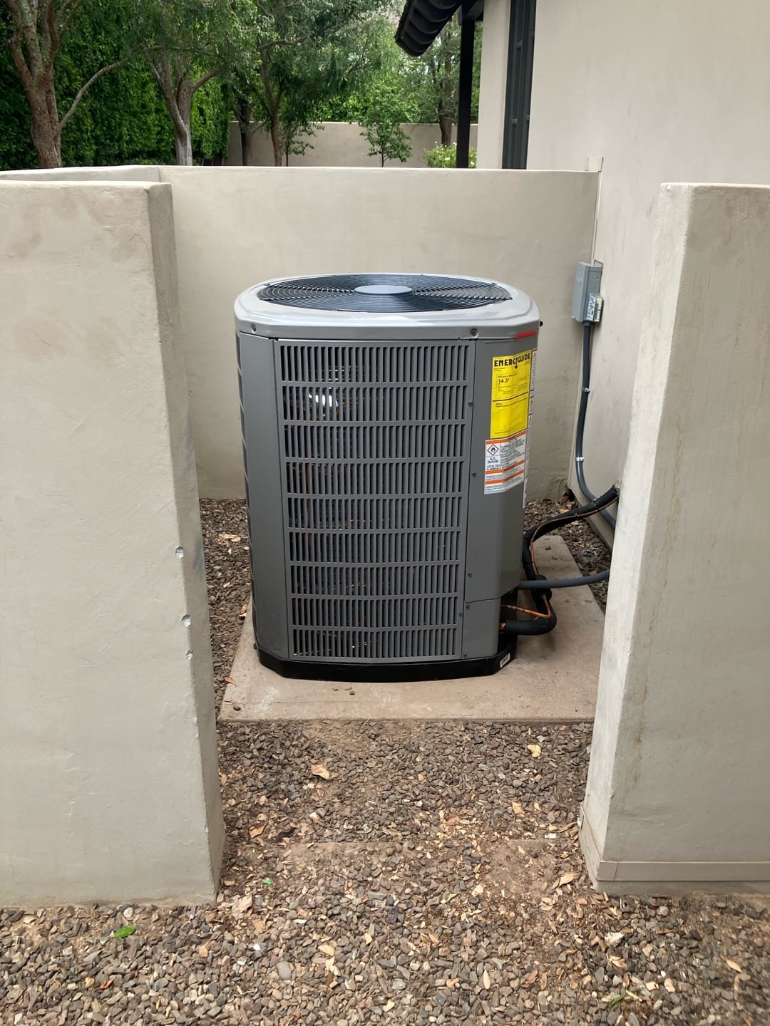 New outdoor condenser set on a level pad with insulated refrigerant lines and exterior disconnect box installed beside the unit.