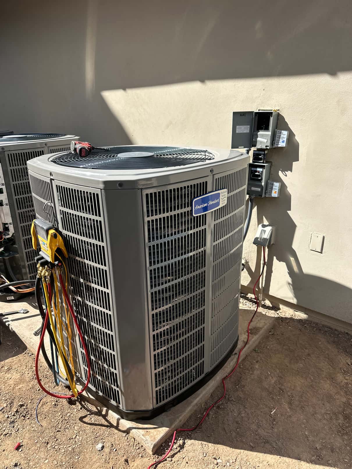 New outdoor condenser set on a level pad with manifold hoses connected and electrical disconnects mounted on the wall nearby.