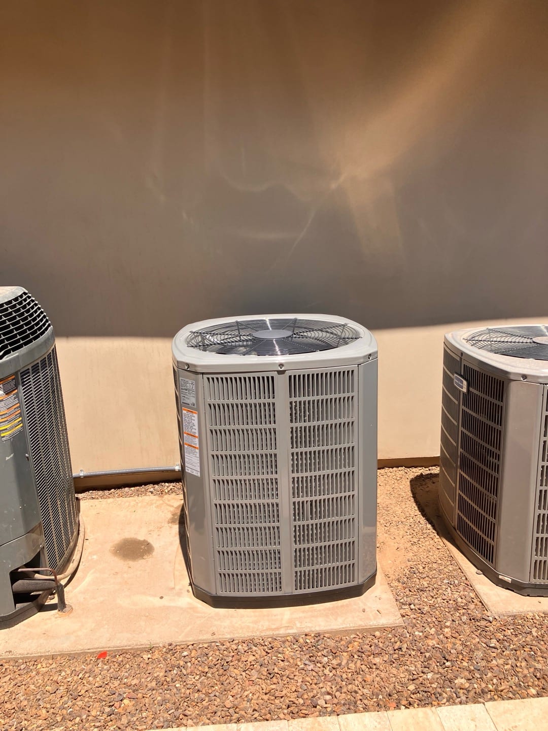 New outdoor condenser set on a level pad with proper clearances, adjacent to existing units along the exterior wall.