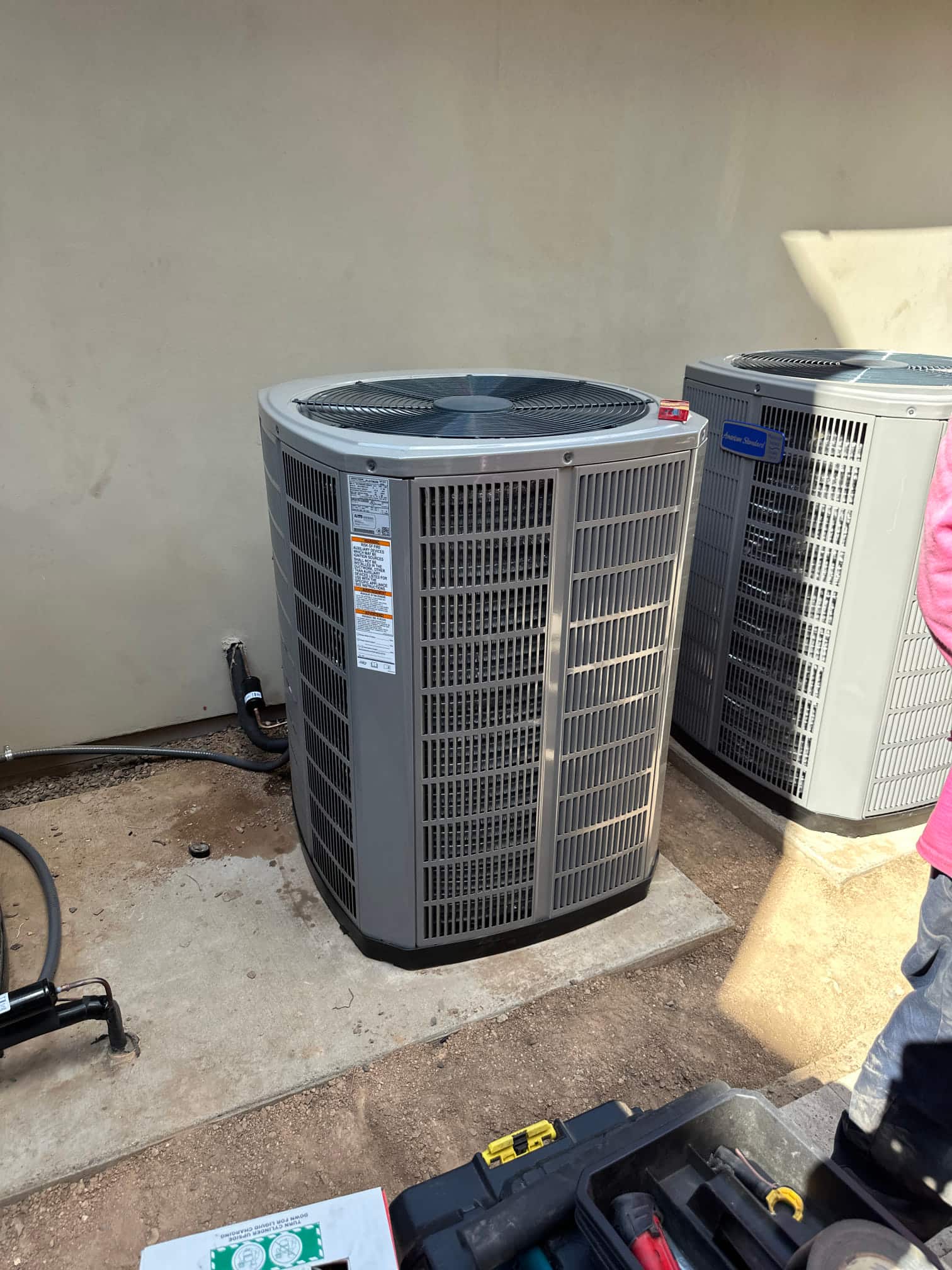New outdoor condenser unit set on a level pad with insulated line set and sealed wall penetration next to existing unit.