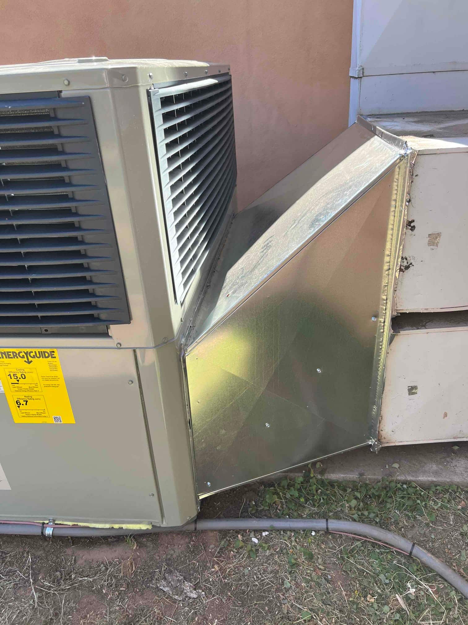 New outdoor unit connected to fabricated galvanized transition duct, sealed and secured on pad with line set routed along the base.