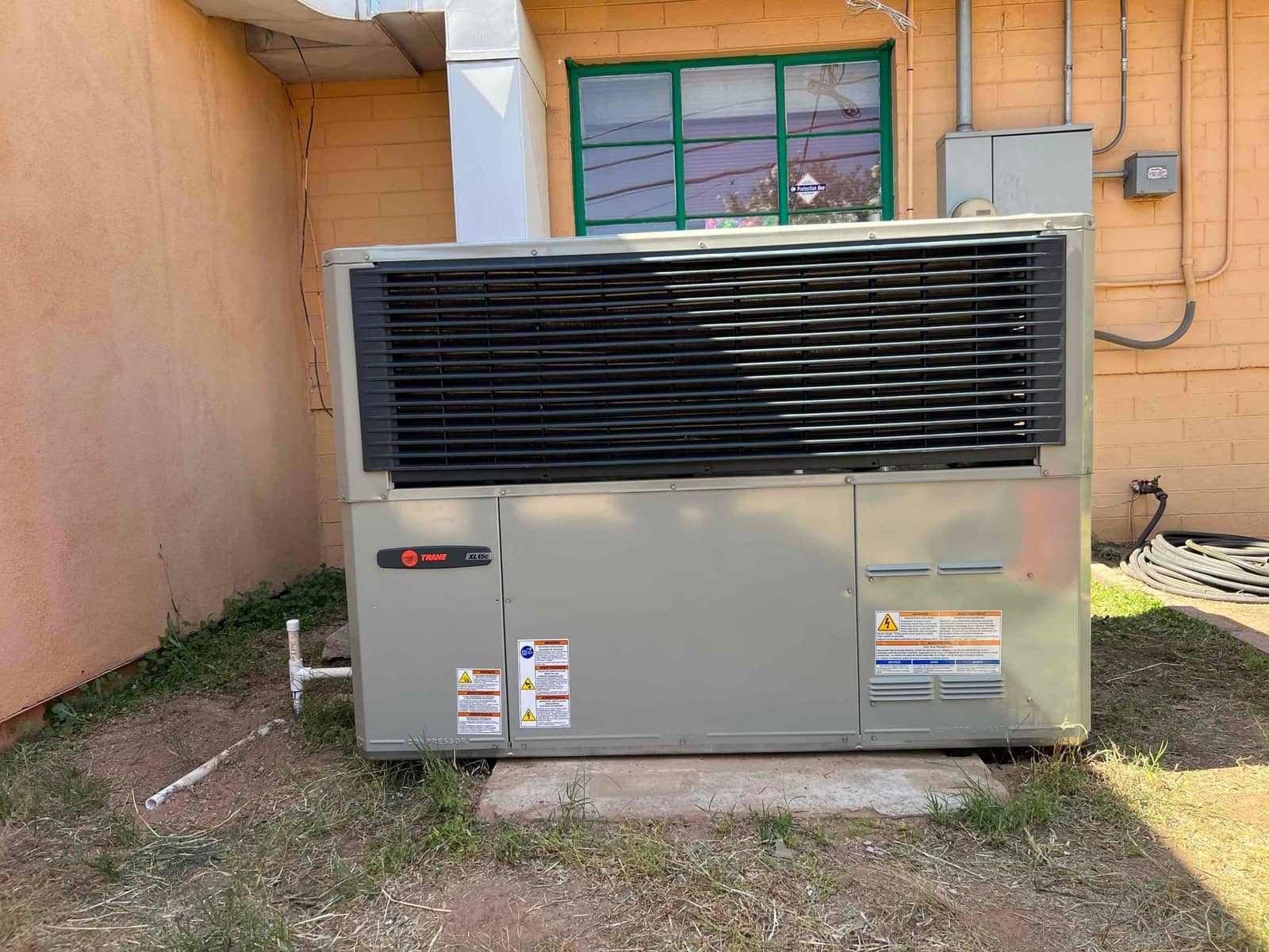 New packaged HVAC unit set outdoors on a level pad with connected condensate drain and sealed duct transition.