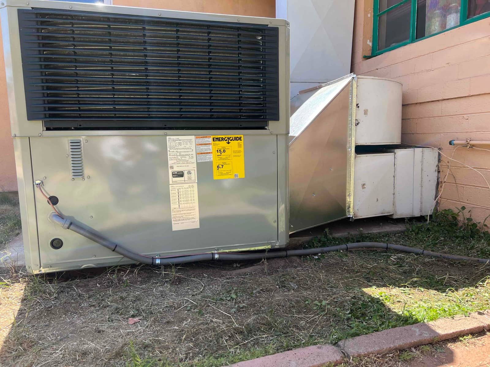 New packaged HVAC unit set outdoors with sealed sheet-metal duct transition and insulated refrigerant line routing along the base.