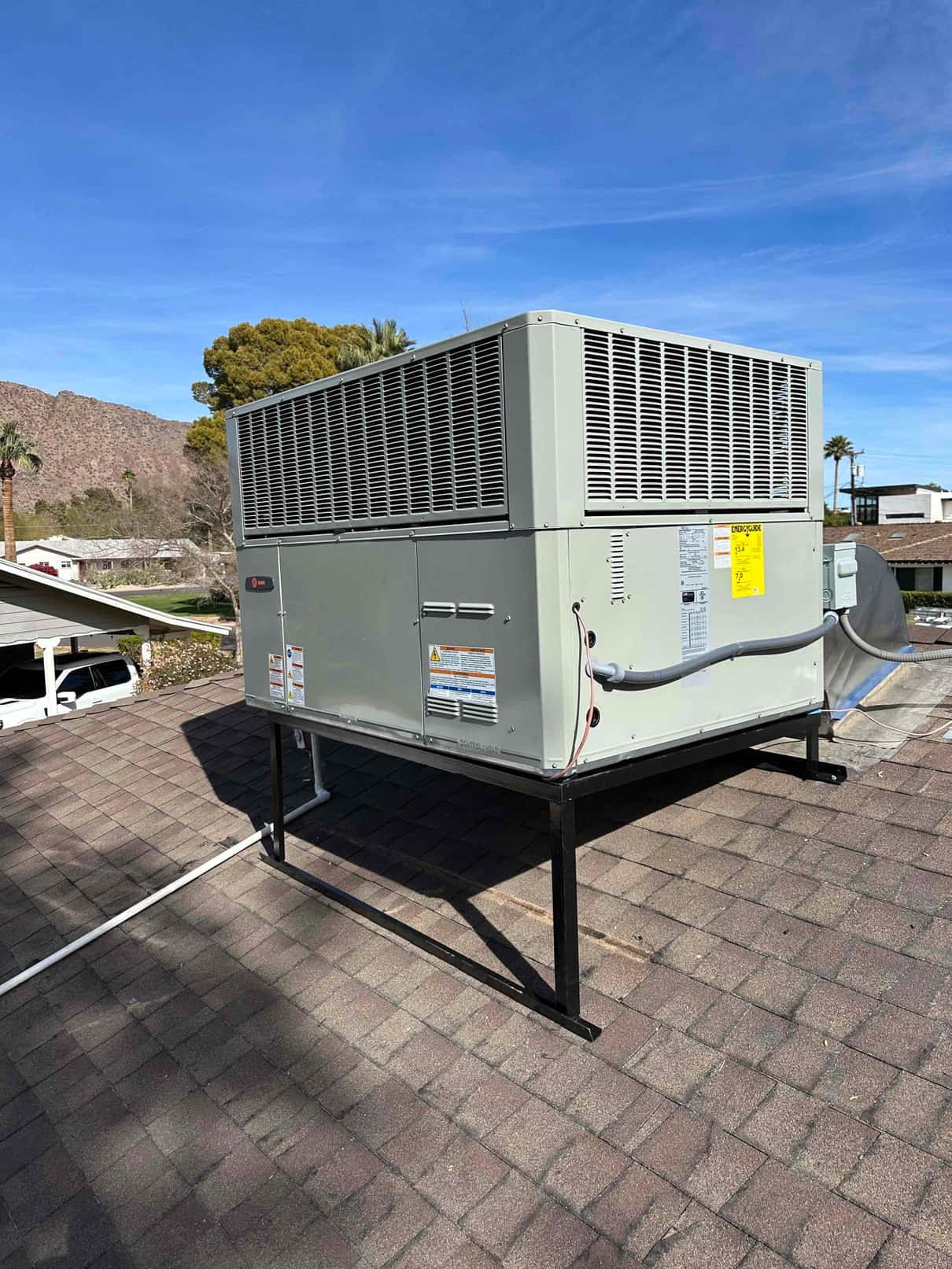 New rooftop packaged HVAC unit installed on a steel stand with connected electrical whip and condensate drain piping.