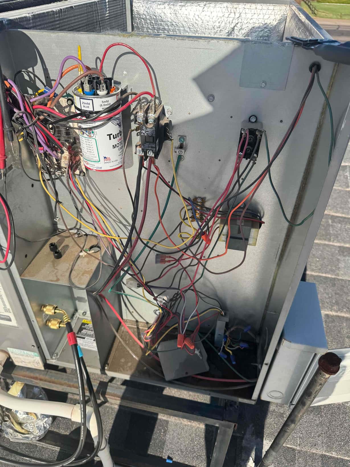 Outdoor condenser control panel open, showing dual-run capacitor, contactor, and wiring during capacitor replacement service.