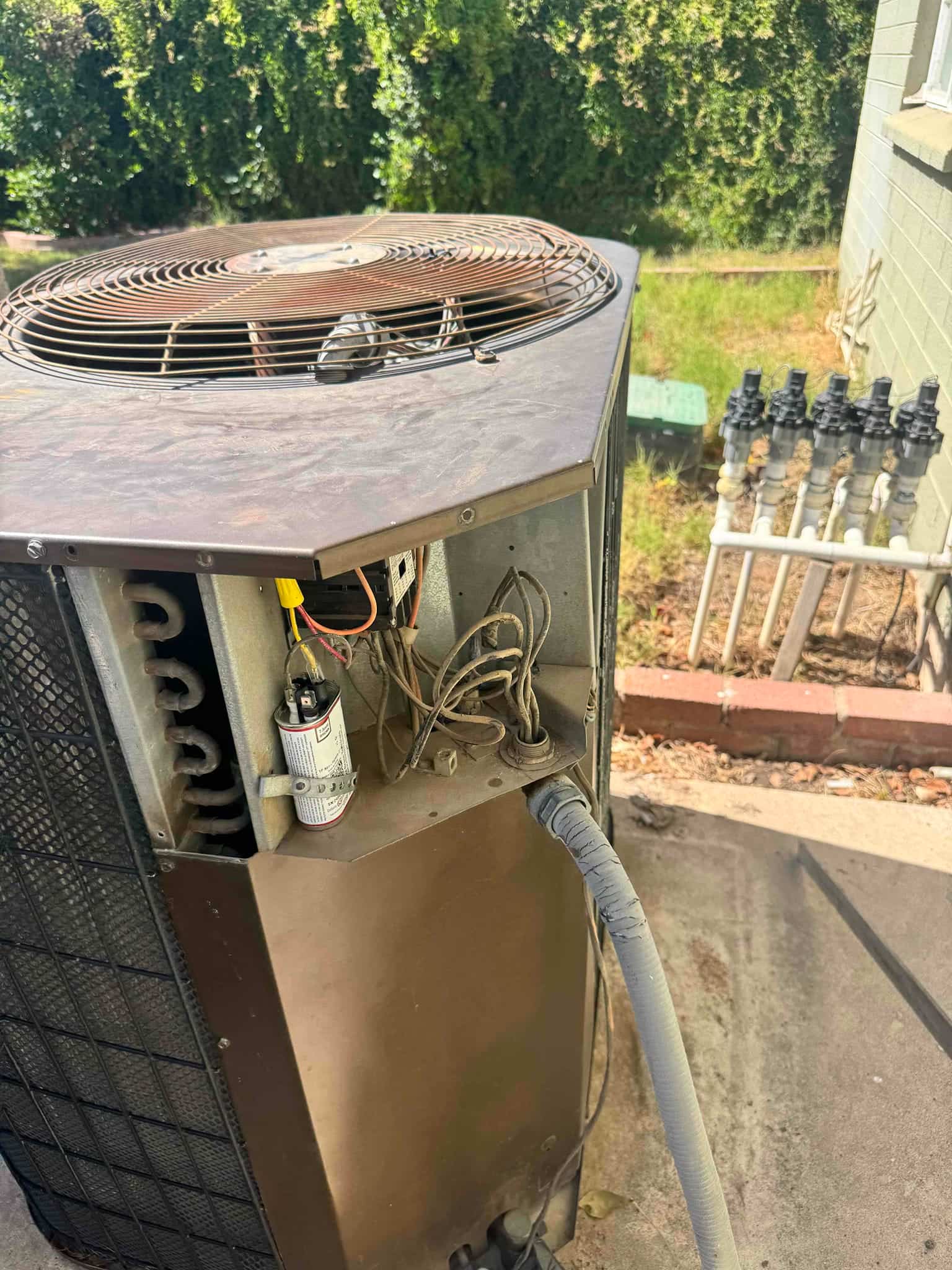 Outdoor condenser with panel open, showing wiring and a new run capacitor installed near the electrical compartment.