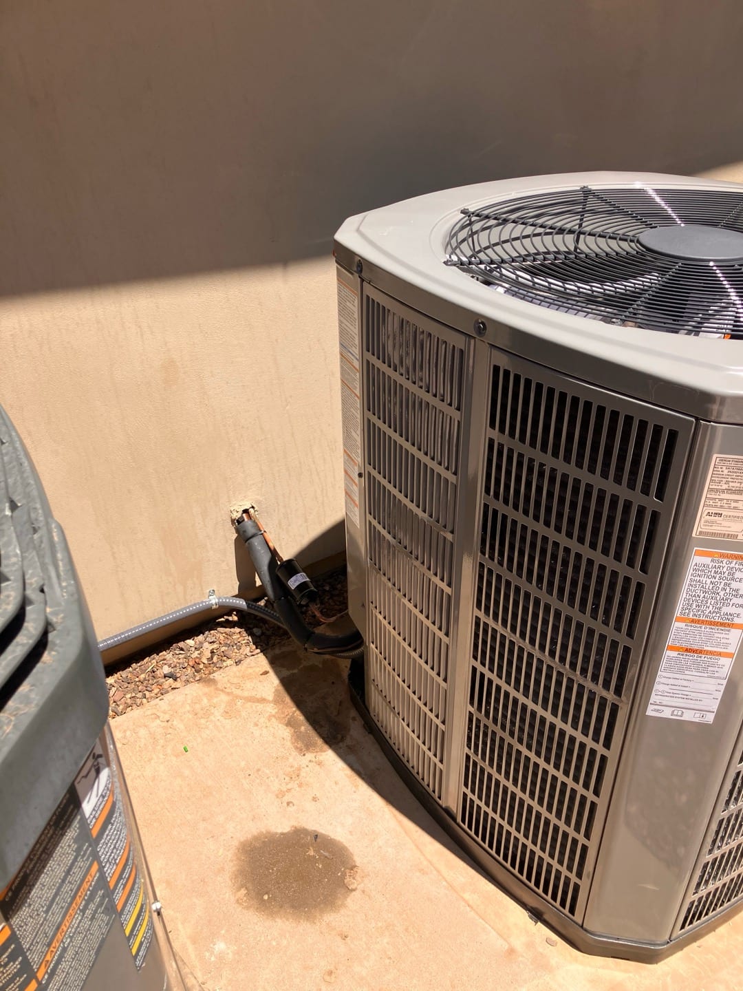 Outdoor condensing unit set on a concrete pad with insulated refrigerant lines and electrical whip routed to the wall penetration.