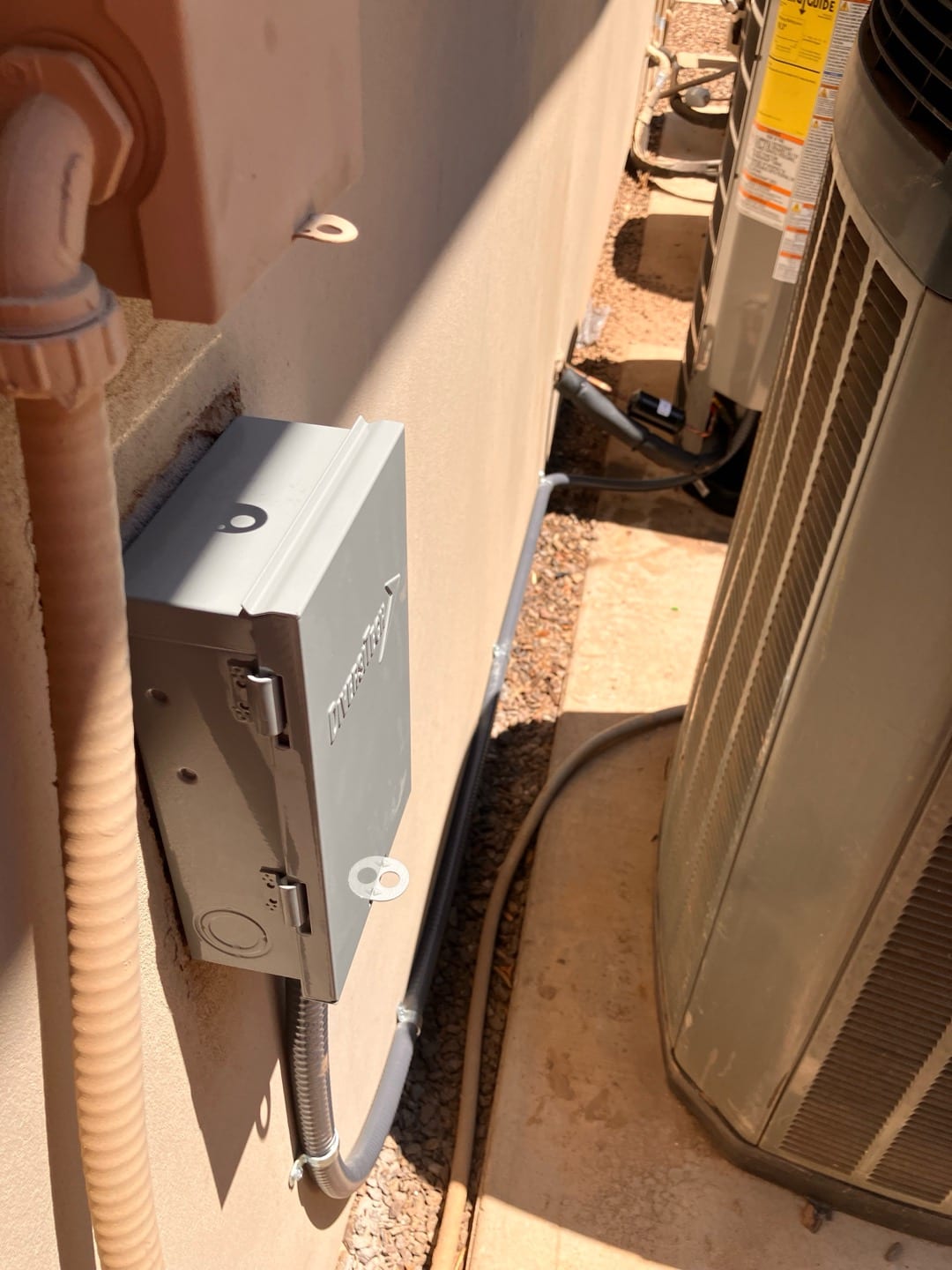 Outdoor disconnect box and flexible conduit installed next to the condenser unit, with secured wiring and sealed wall penetration.