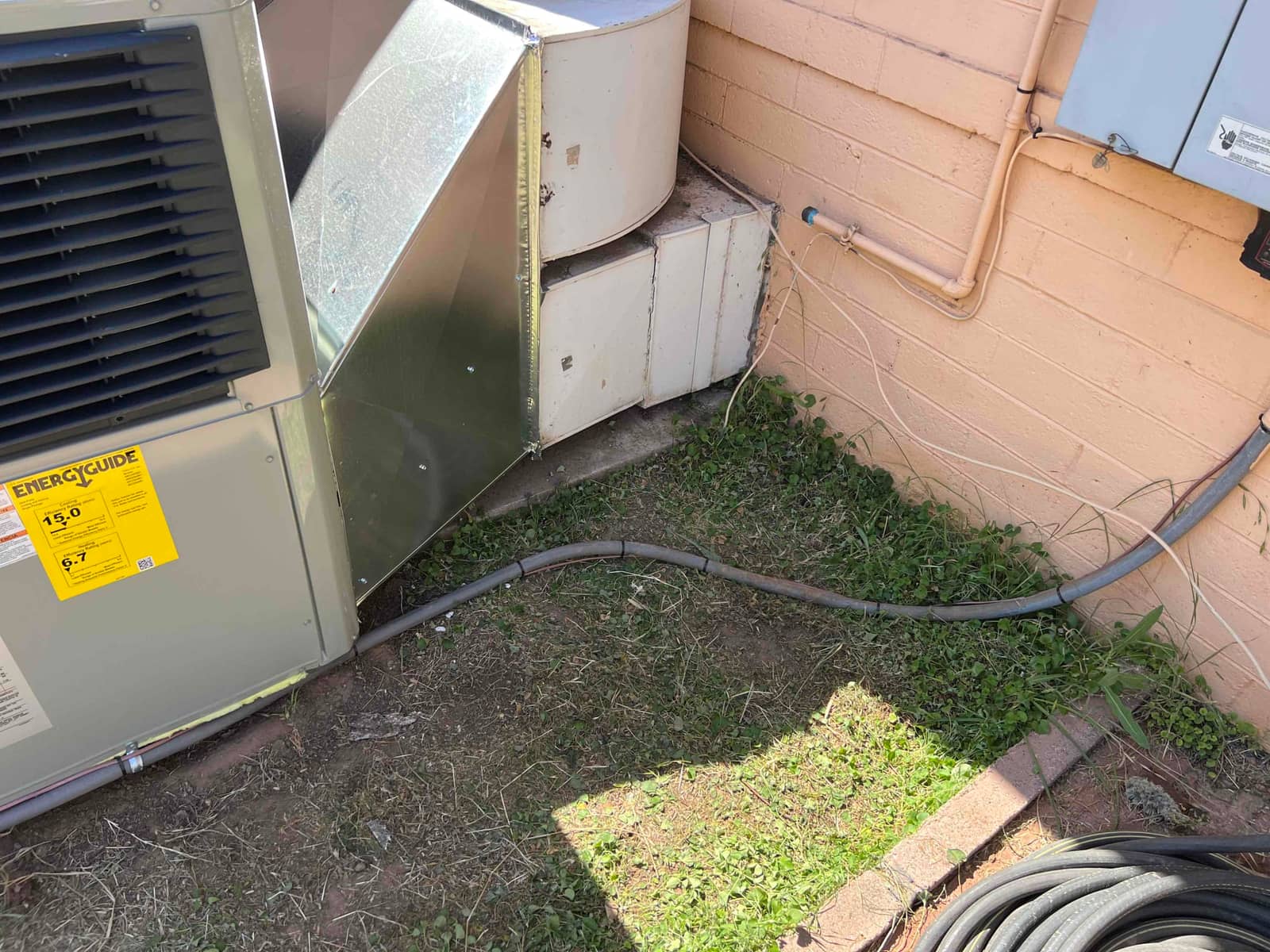 Outdoor heat pump set on pad with new sheet-metal transition to existing ductwork and sealed electrical conduit along wall.