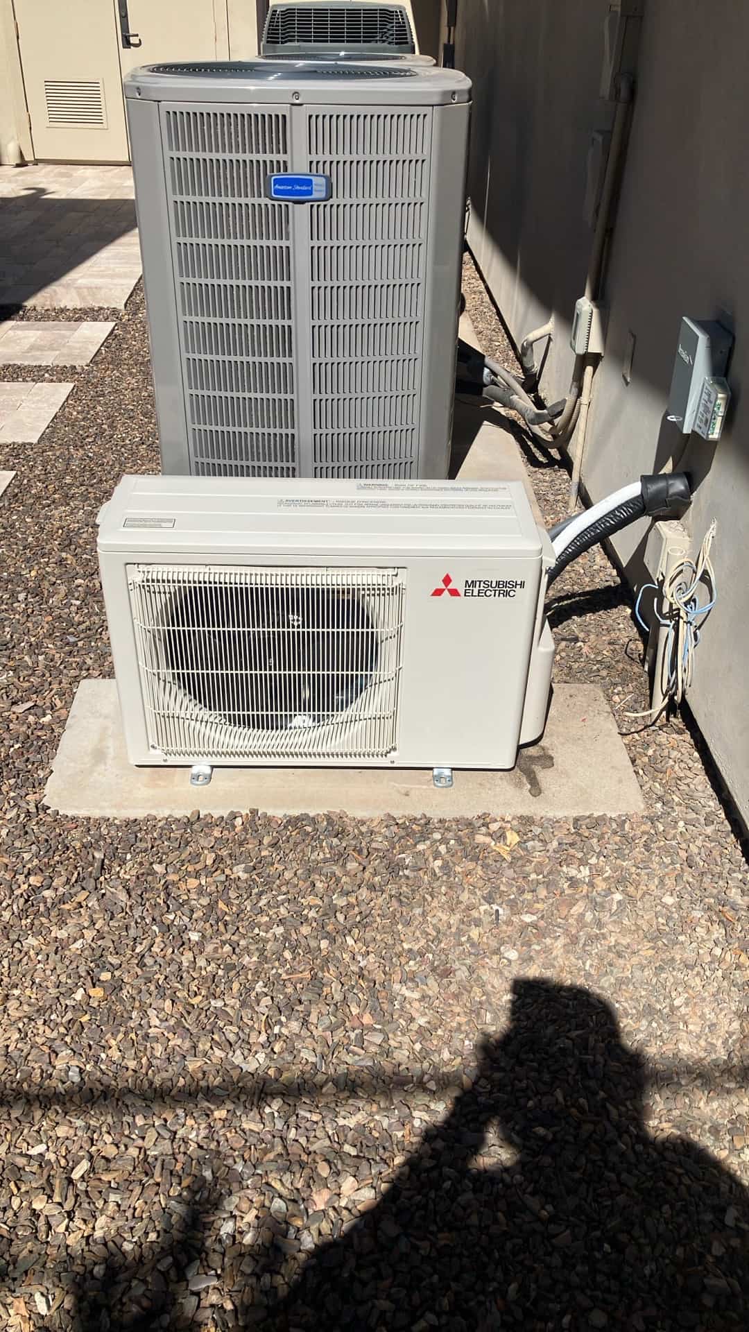 Two outdoor HVAC units set on level pads with insulated line sets and electrical disconnects mounted on the wall.