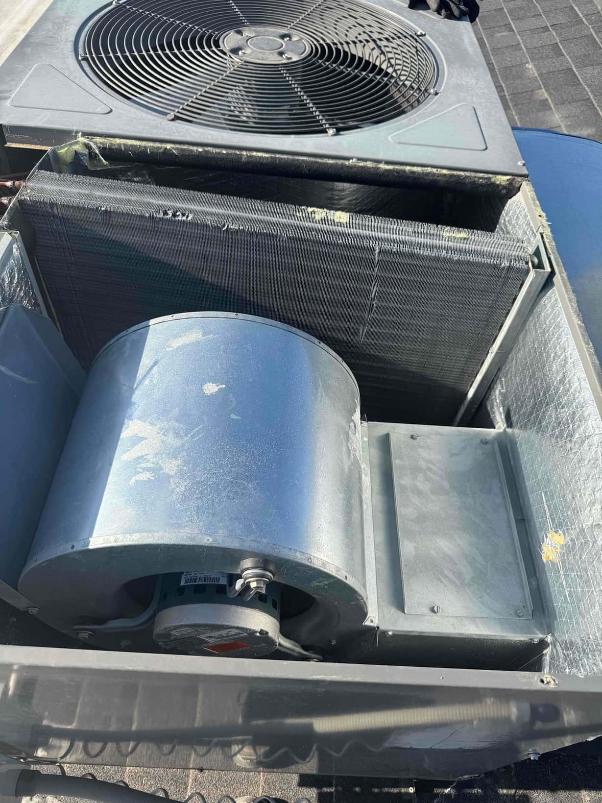 Outdoor package unit with condenser coil exposed and blower housing visible during air conditioning repair on the rooftop.
