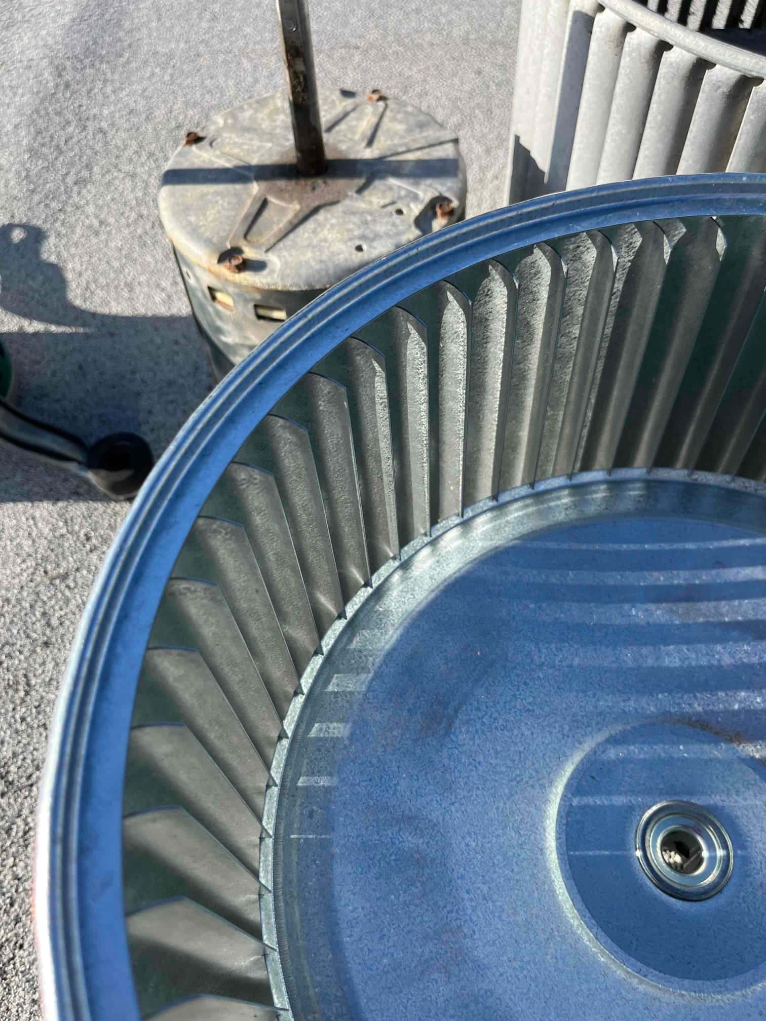 Removed blower wheels and an old ECM blower motor sit on the ground, showing clean fins and central hub detail.