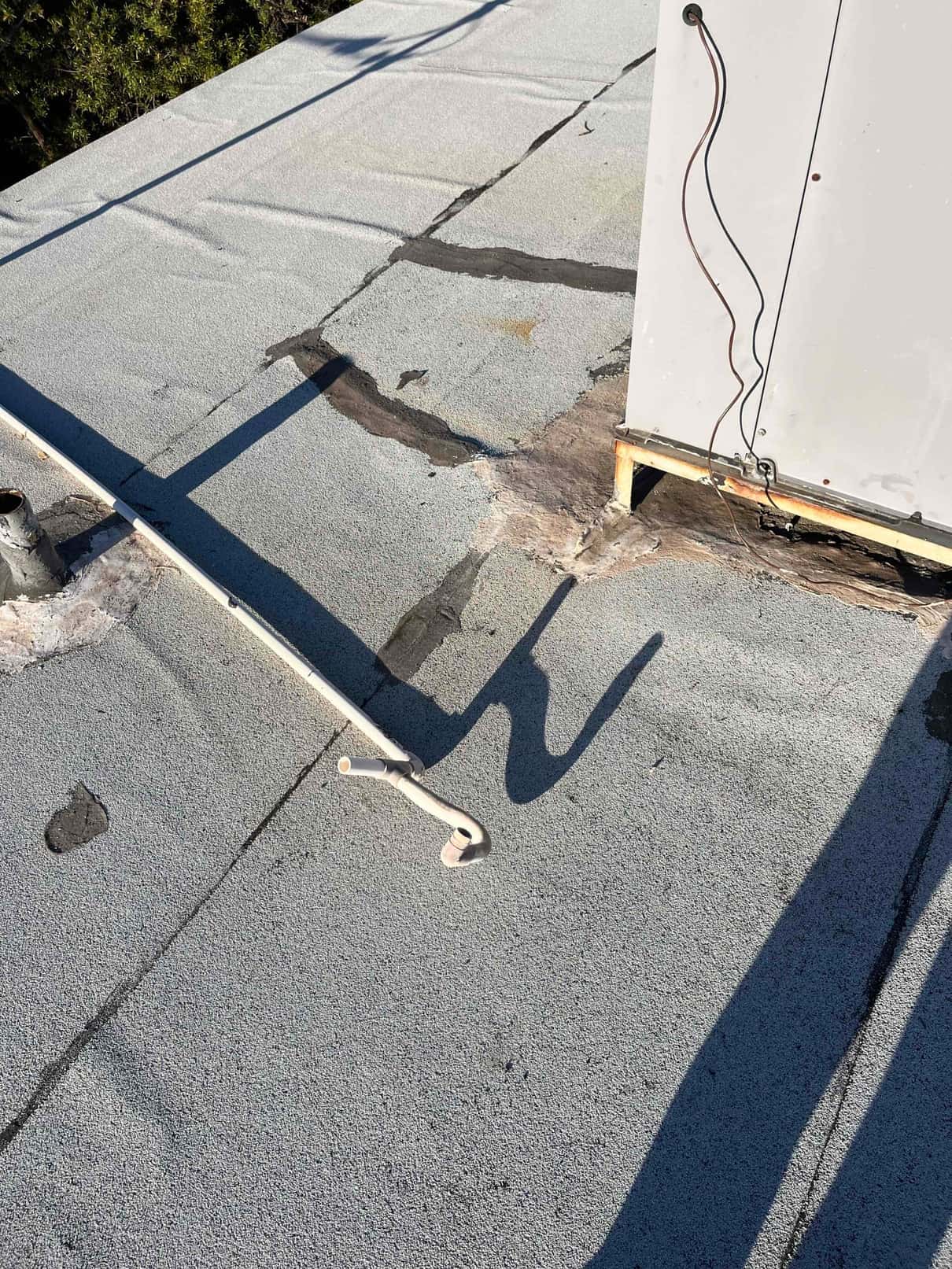 Rooftop air conditioning unit with exposed control wires and nearby roof repair patches around the curb and penetration.