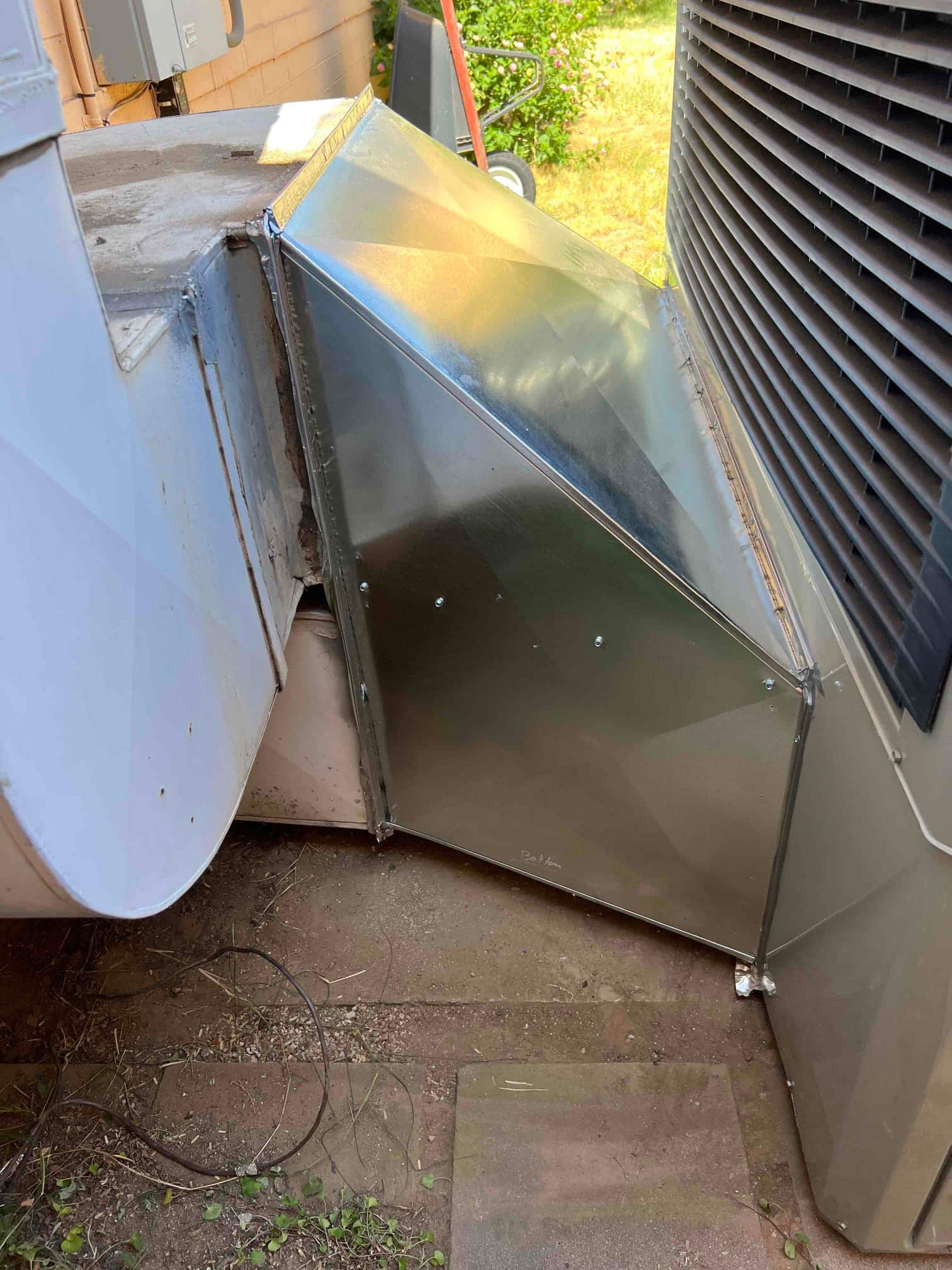 Sheet-metal transition duct connects the new outdoor package unit to existing ductwork, with sealed joints and proper alignment on the pad.