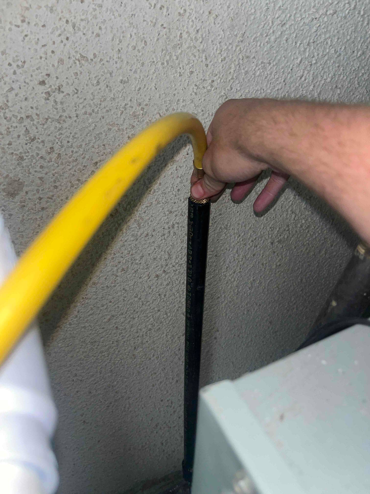 Technician feeds a yellow hose into a black condensate drain line to clear a blockage during repair.