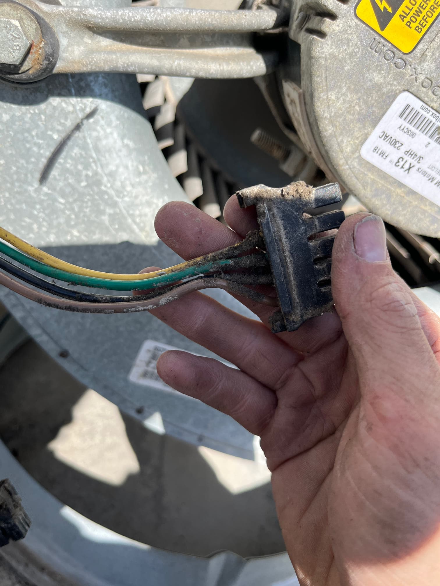 Technician holds a dusty multi-pin electrical connector with colored wires near the blower motor and wheel assembly.