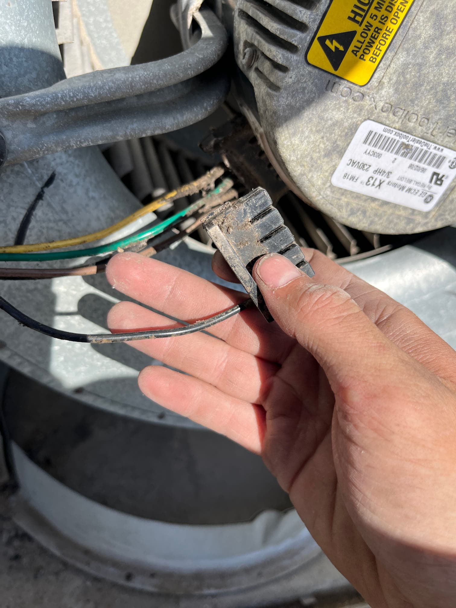 Technician holds a worn blower motor wiring connector with exposed wires near the blower assembly and motor housing.