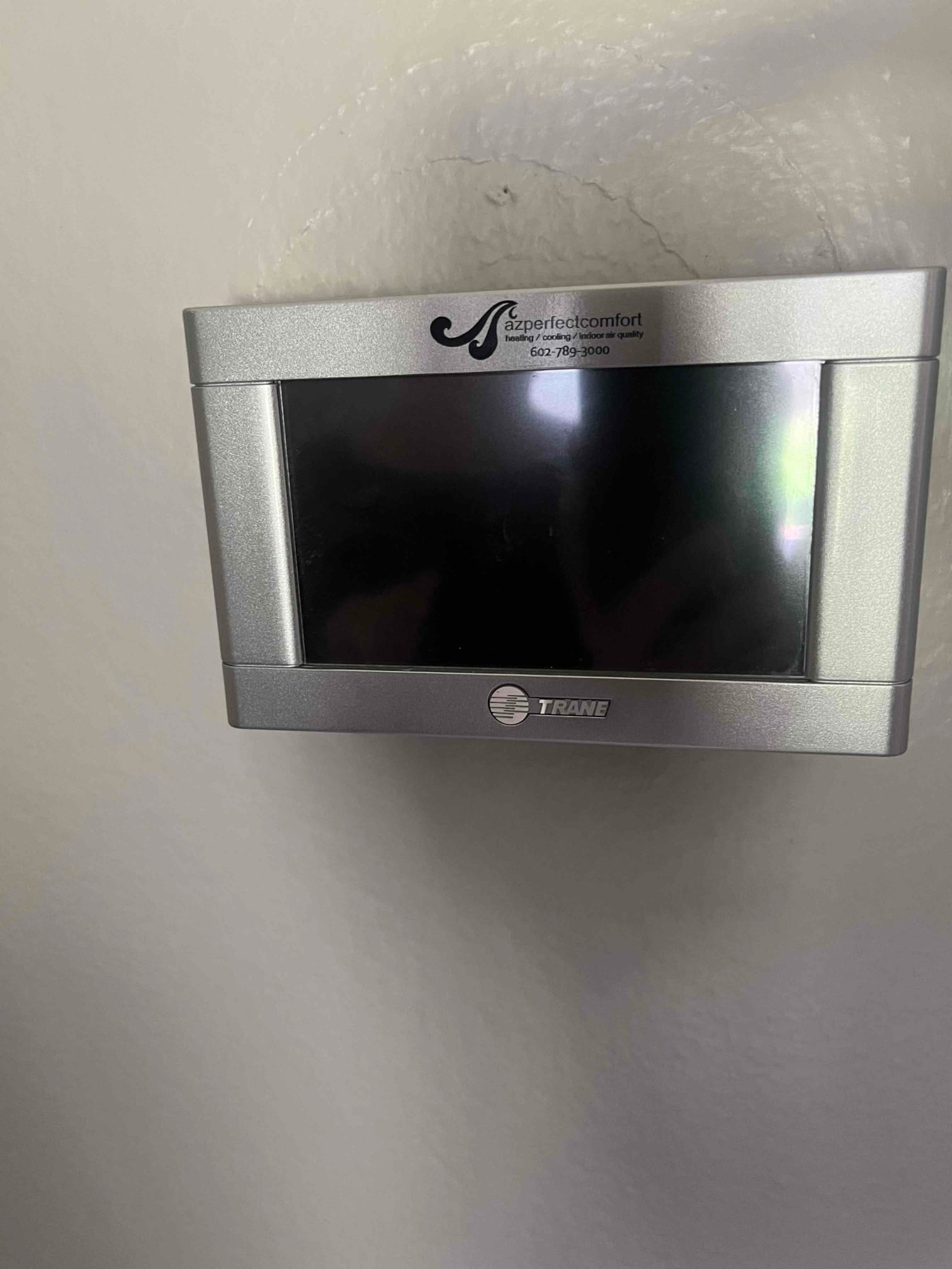 Wall-mounted digital thermostat with a blank black display screen and surrounding silver housing on an indoor wall.