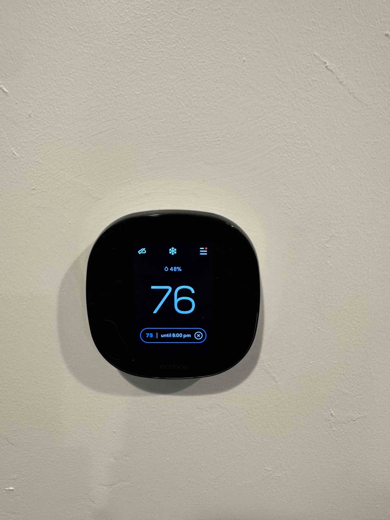 Wall-mounted smart thermostat display shows room temperature at 76°F with cooling setpoint active on the screen.