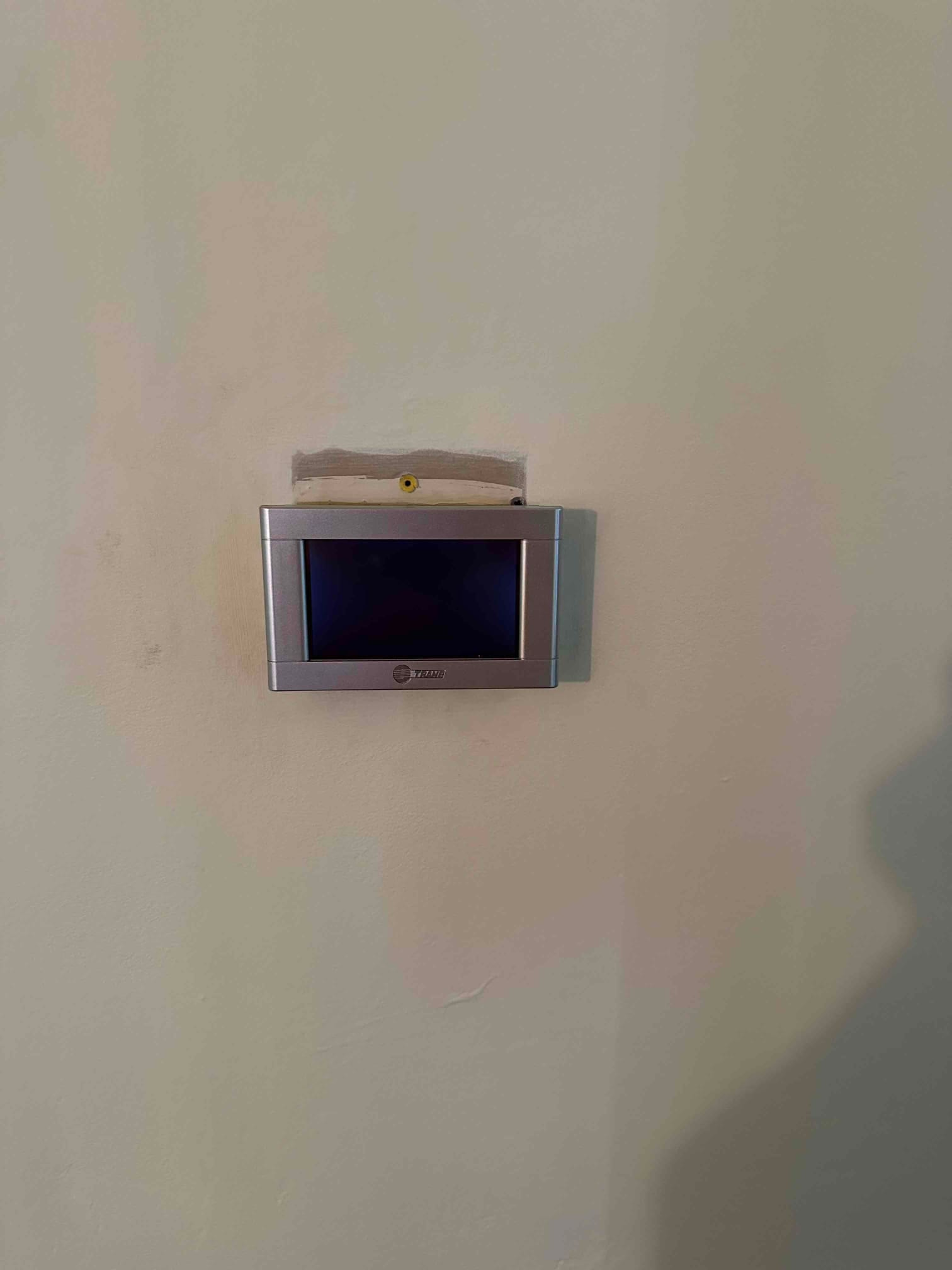 Wall-mounted thermostat installed with finished wall repair above, ready for system configuration and homeowner use.