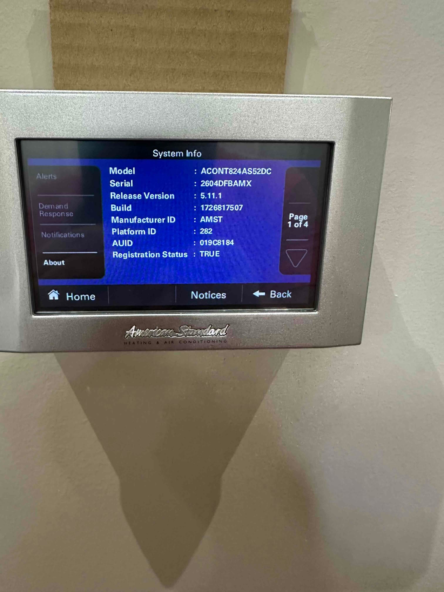 Wall-mounted touchscreen thermostat displays system information menu after installation, confirming control interface operation and connectivity.