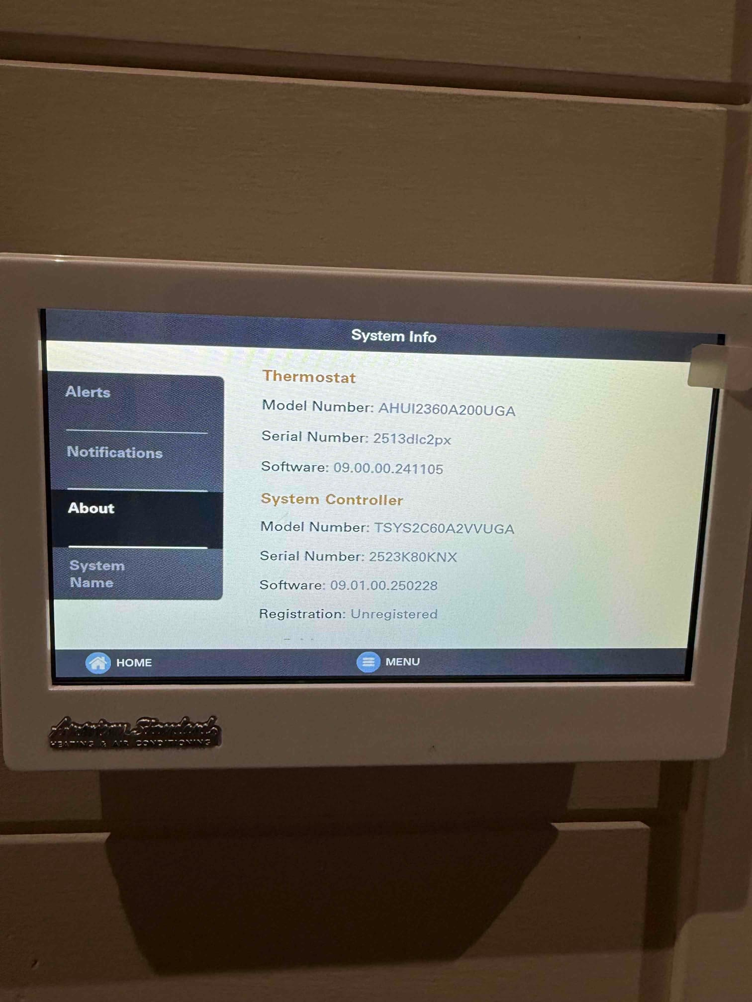 Wall-mounted touchscreen thermostat displays system information screen after installation, showing menu navigation and setup interface.